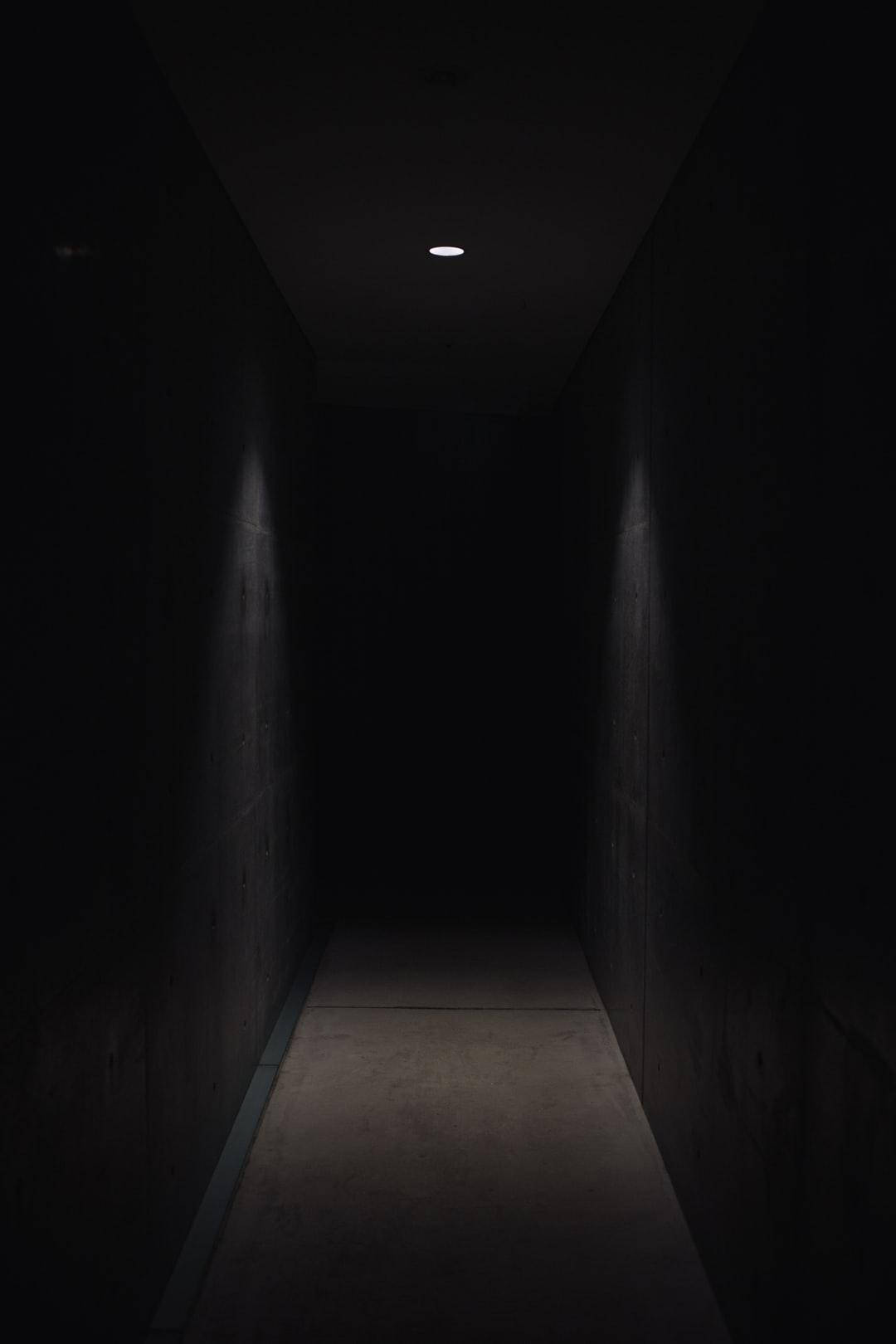 1080p HD 桌布 壁紙 — 一條狹窄的混凝土走廊陷入黑暗，僅由一盞頭頂燈照亮，投下長長的陰影。