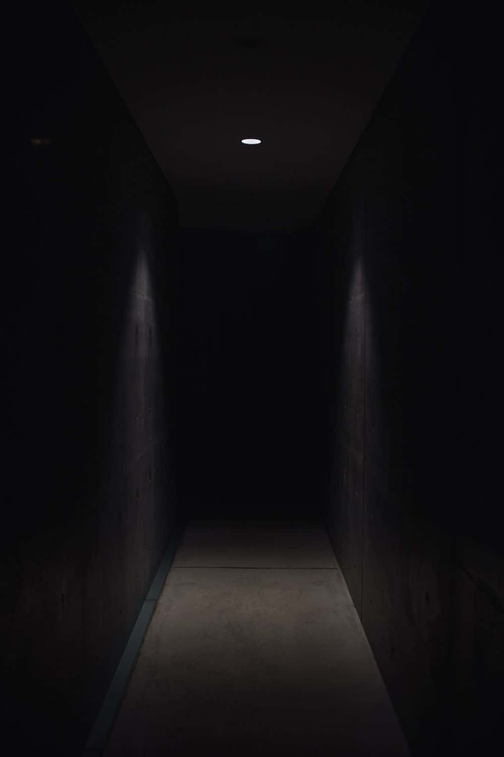 Dark Scary 桌布 壁紙 — 一條狹窄的混凝土走廊陷入黑暗，僅由一盞頭頂燈照亮，投下長長的陰影。