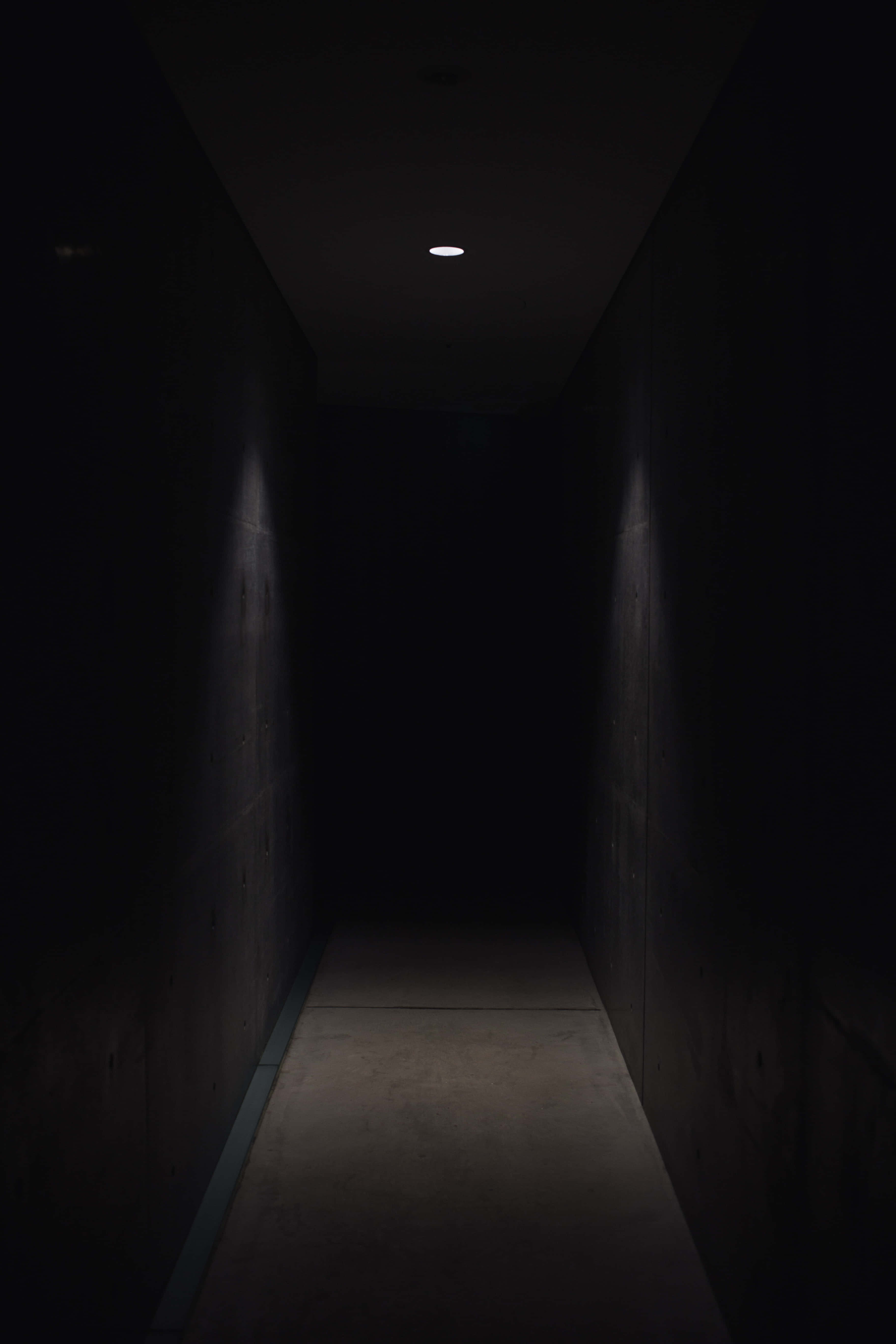 hallway 桌布 壁紙 — 一條狹窄的混凝土走廊陷入黑暗，僅由一盞天花燈照亮，投下長長的陰影。