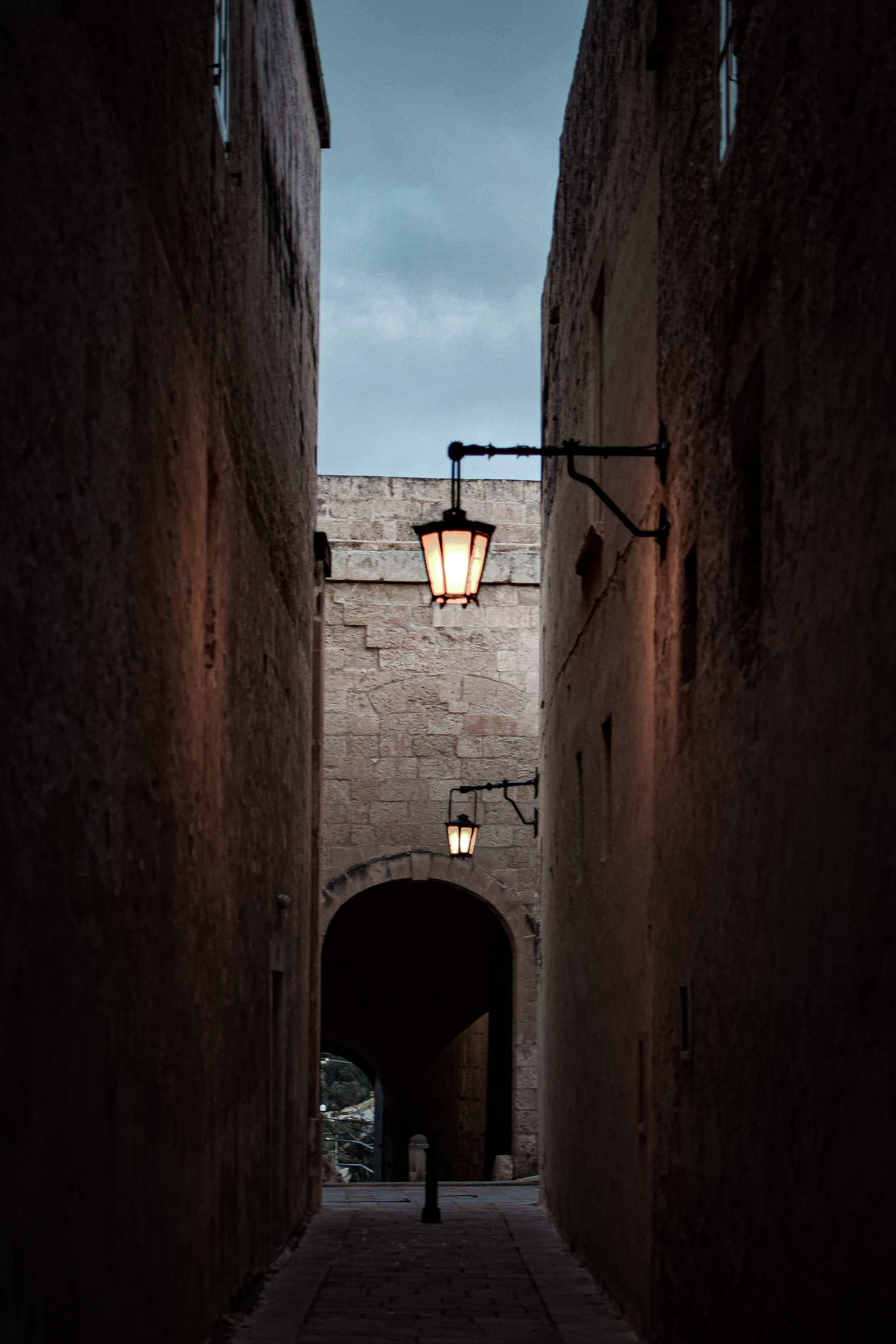 Malta 桌布 壁紙 — 一條狹窄的石巷在黃昏時分，被溫暖的復古燈籠照亮，映襯著憂鬱的暮色天空。