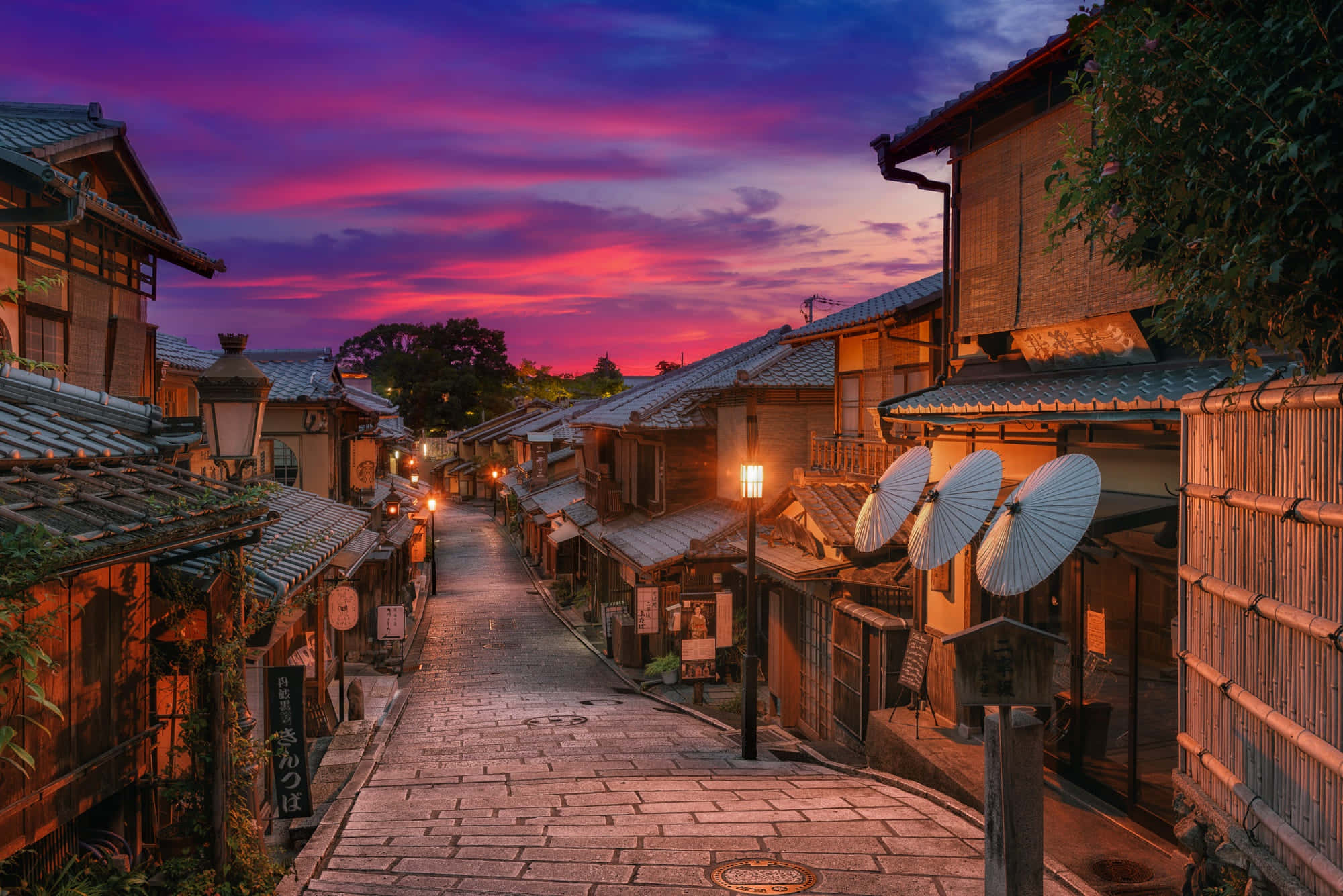 日本 桌布 壁紙 — 一條狹窄的石頭街道，兩旁是傳統木建築，上方是充滿活力的粉紅色和紫色黃昏天空。