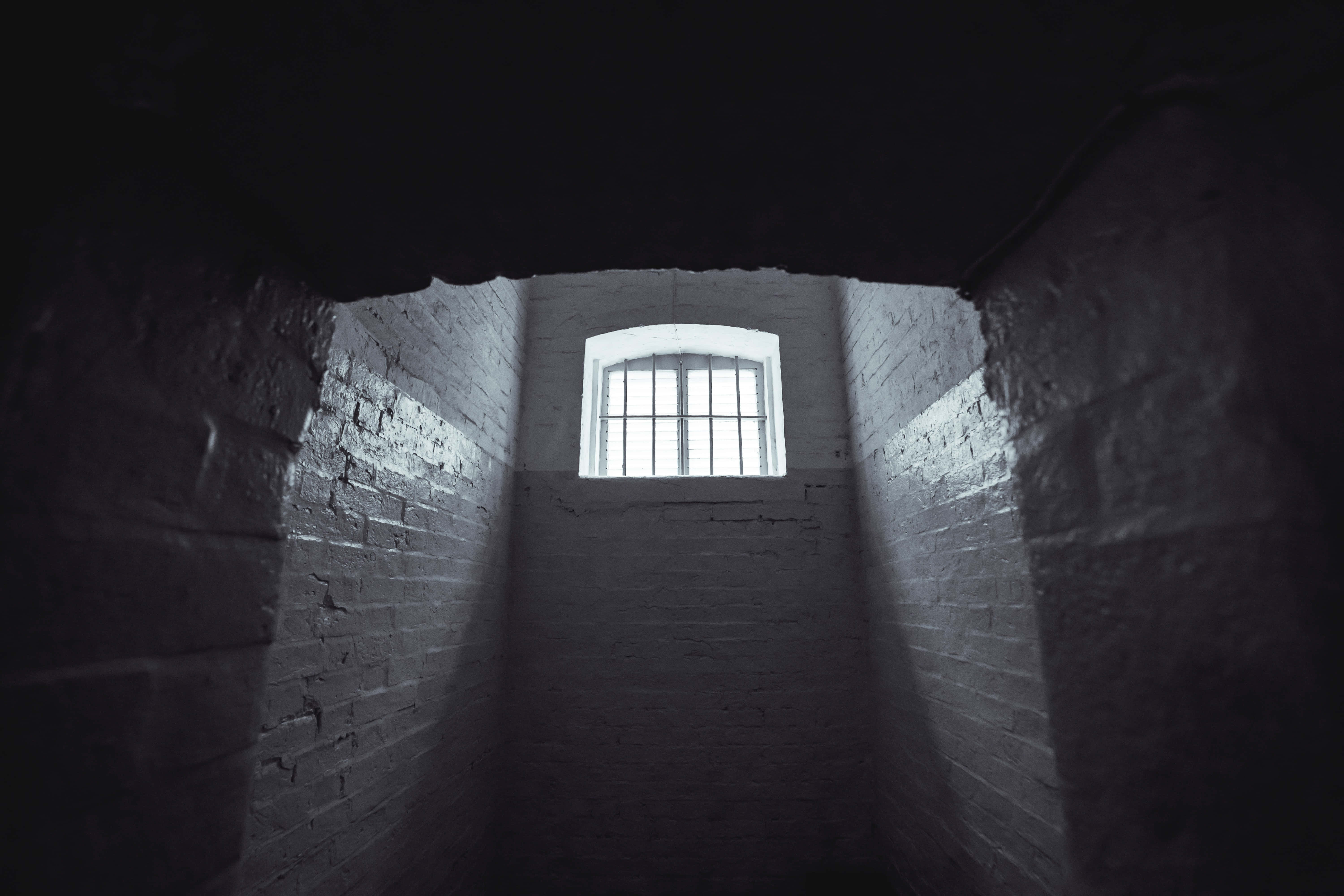 Dark Room 桌布 壁紙 — 一條狹窄的磚砌隧道通向帶有鐵欄的窗戶，將強烈的光線投射到陰暗封閉的空間中。