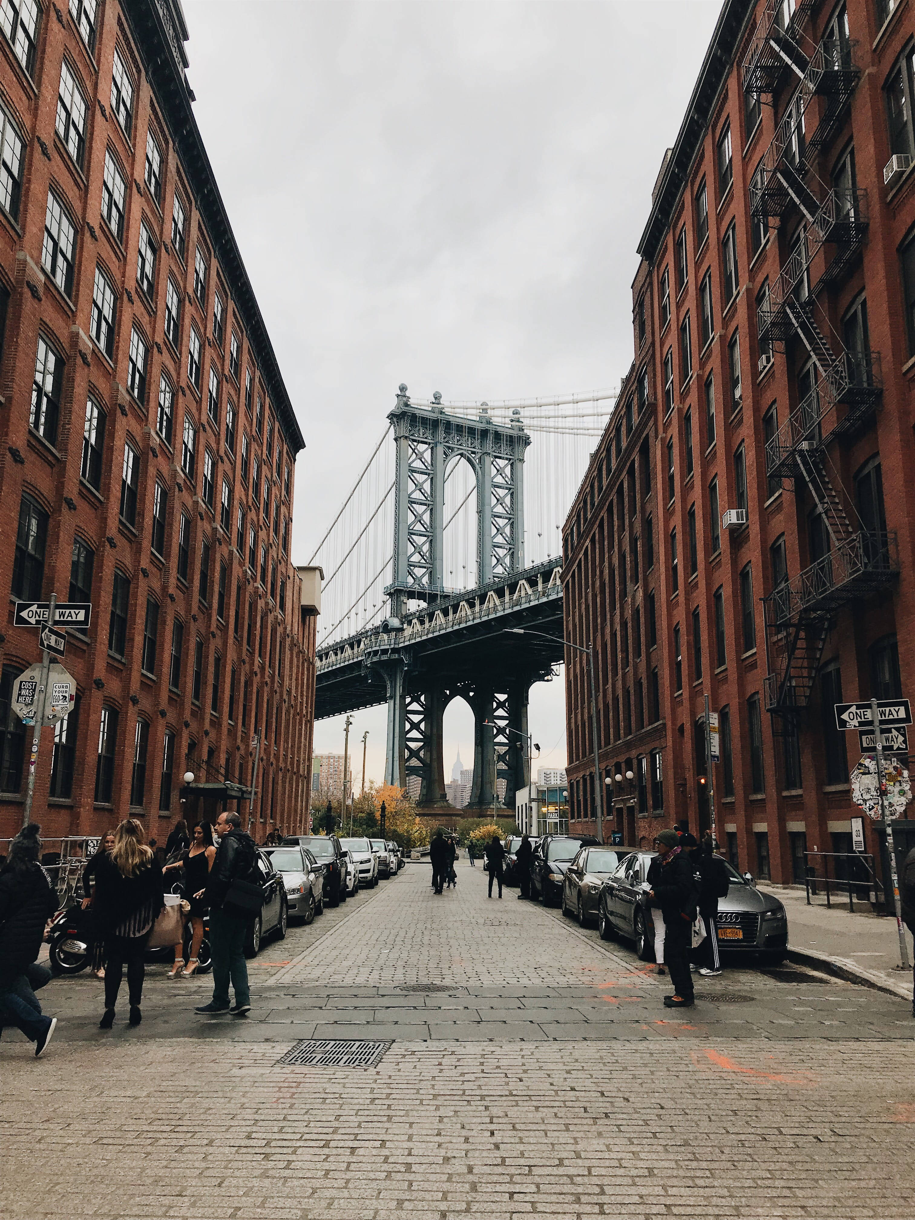 Brooklyn Bridge 桌布 壁紙 — 一條狹窄的磚街，兩旁是紅磚建築，在陰天之下通往標誌性的曼哈頓大橋。