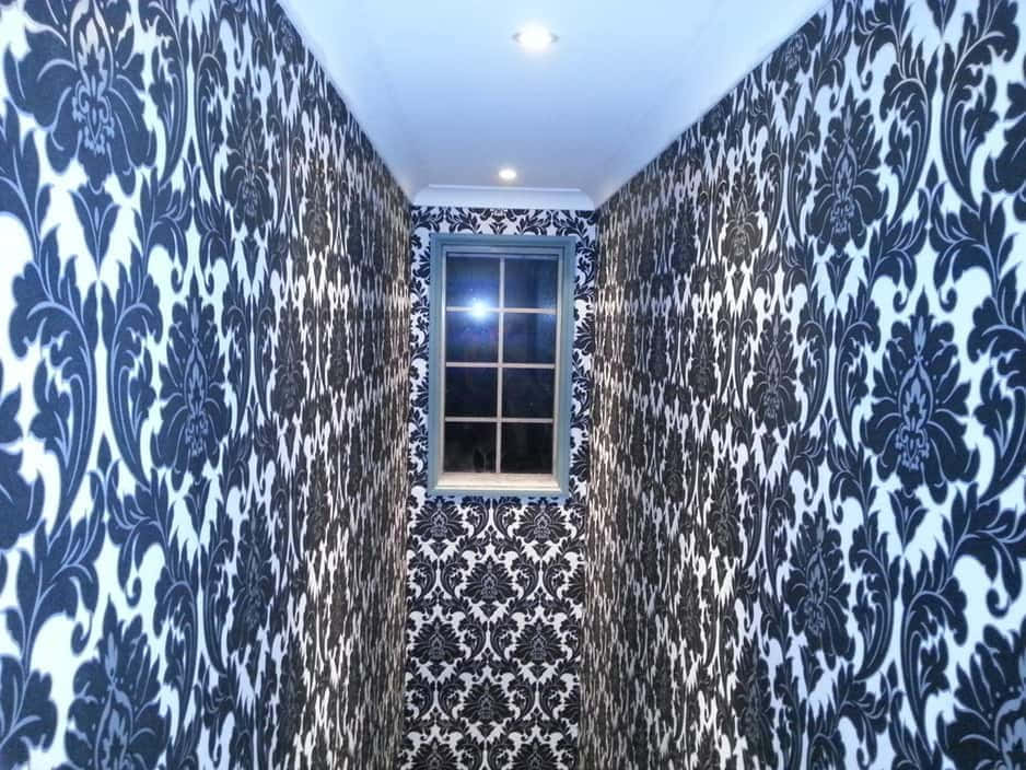 Installation Art 桌布 壁紙 — 一條狹窄的走廊，鋪有華麗的黑白大馬士革壁紙，在明亮的吊燈下向著一扇小窗戶收窄。