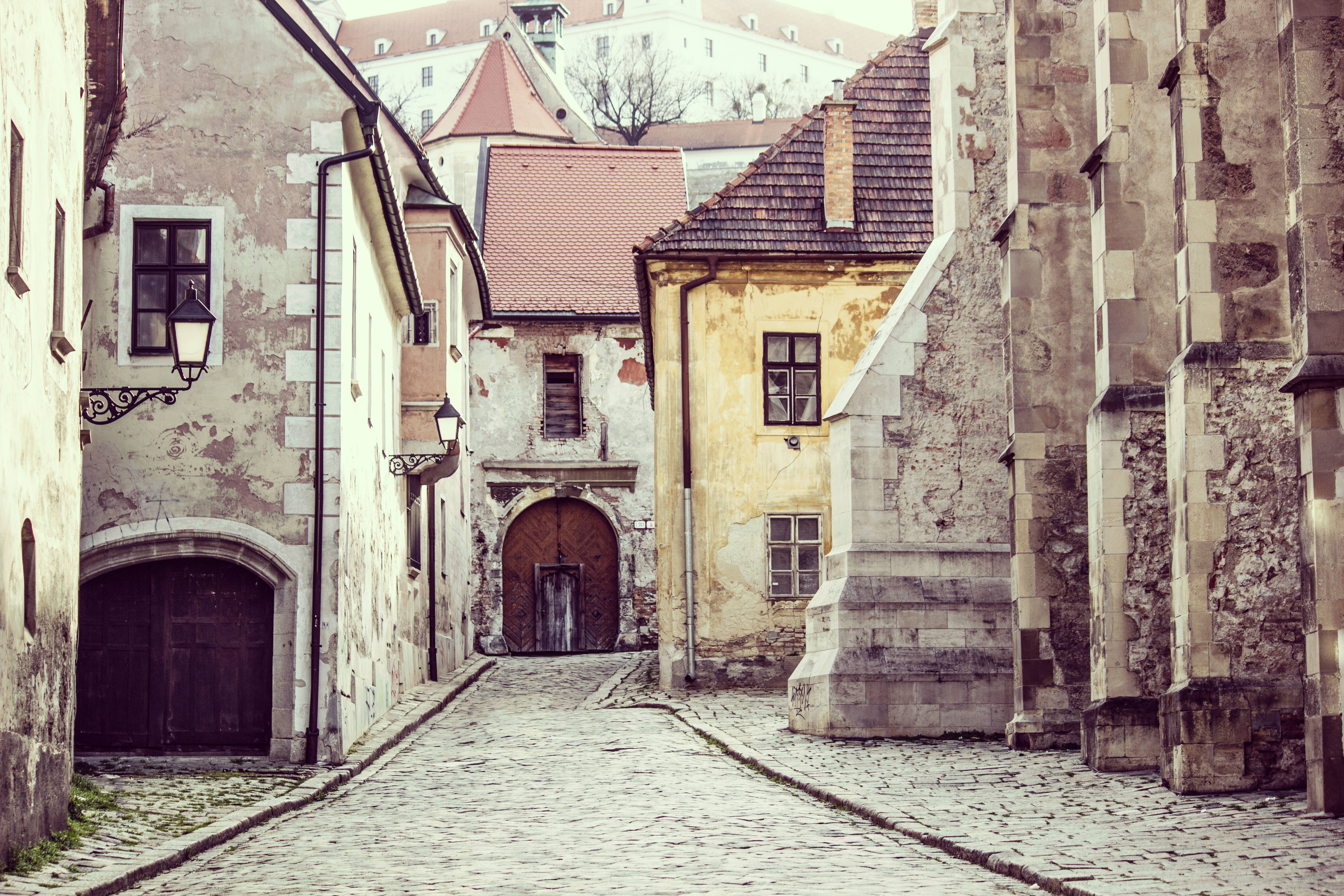 Slovakia 桌布 壁紙 — 一條狹窄的鵝卵石小巷，兩旁是歷經風霜的歷史建築，在柔和日光下。