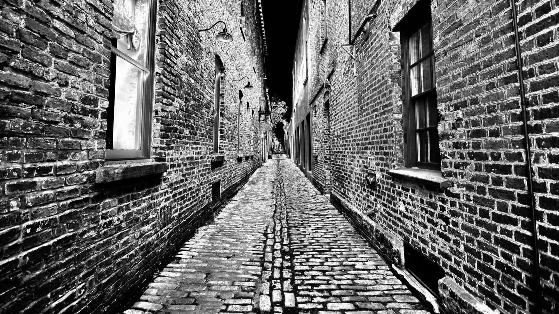 Alleyway 桌布 壁紙 — 一條狹窄的鵝卵石小巷，兩旁是風化的磚砌建築，在高高的天空下延伸至黑暗的遠方。