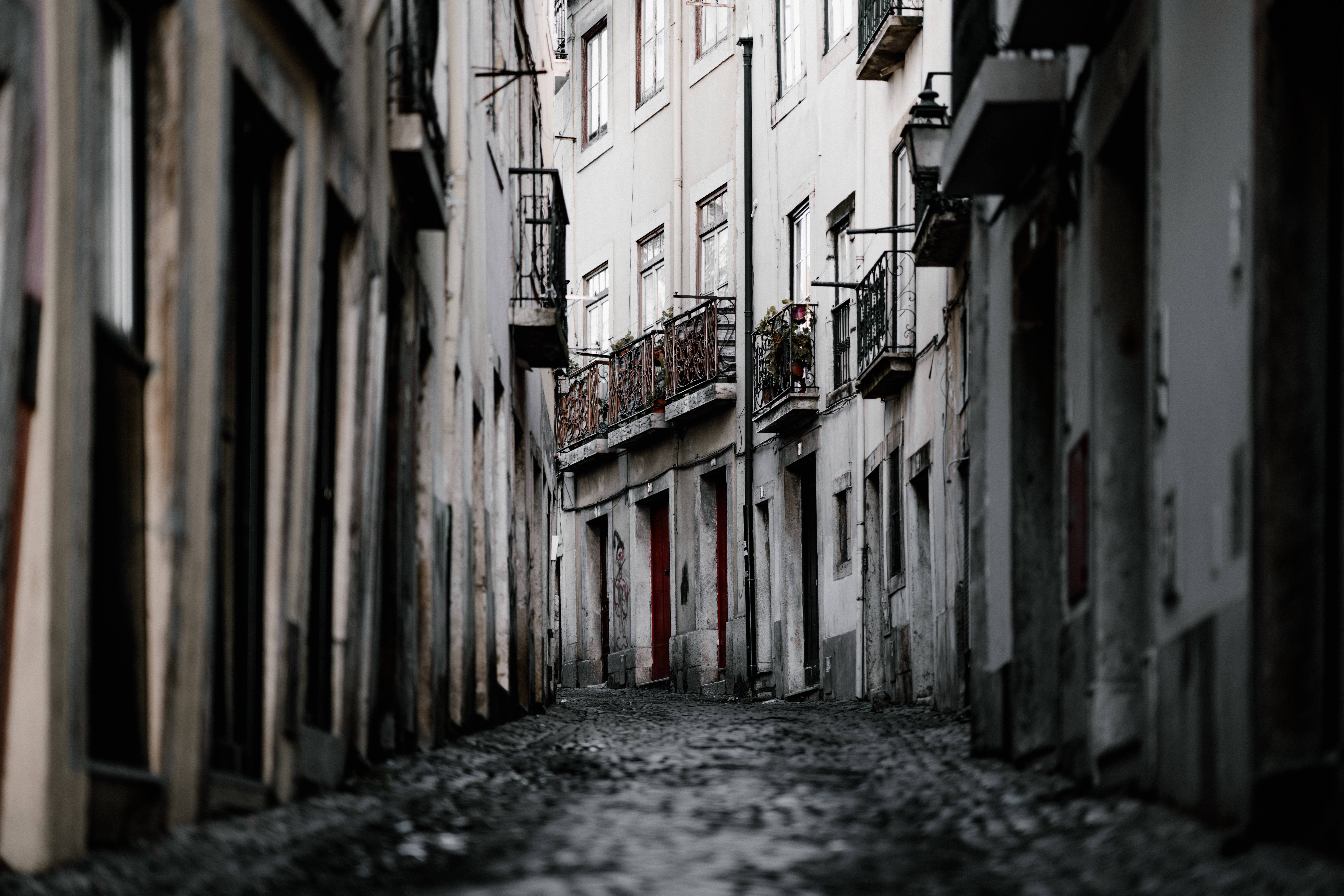 Portugal 桌布 壁紙 — 一條狹窄的鵝卵石小巷，兩旁是風化的歐洲建築，帶有華麗的陽台和一扇紅色的門。