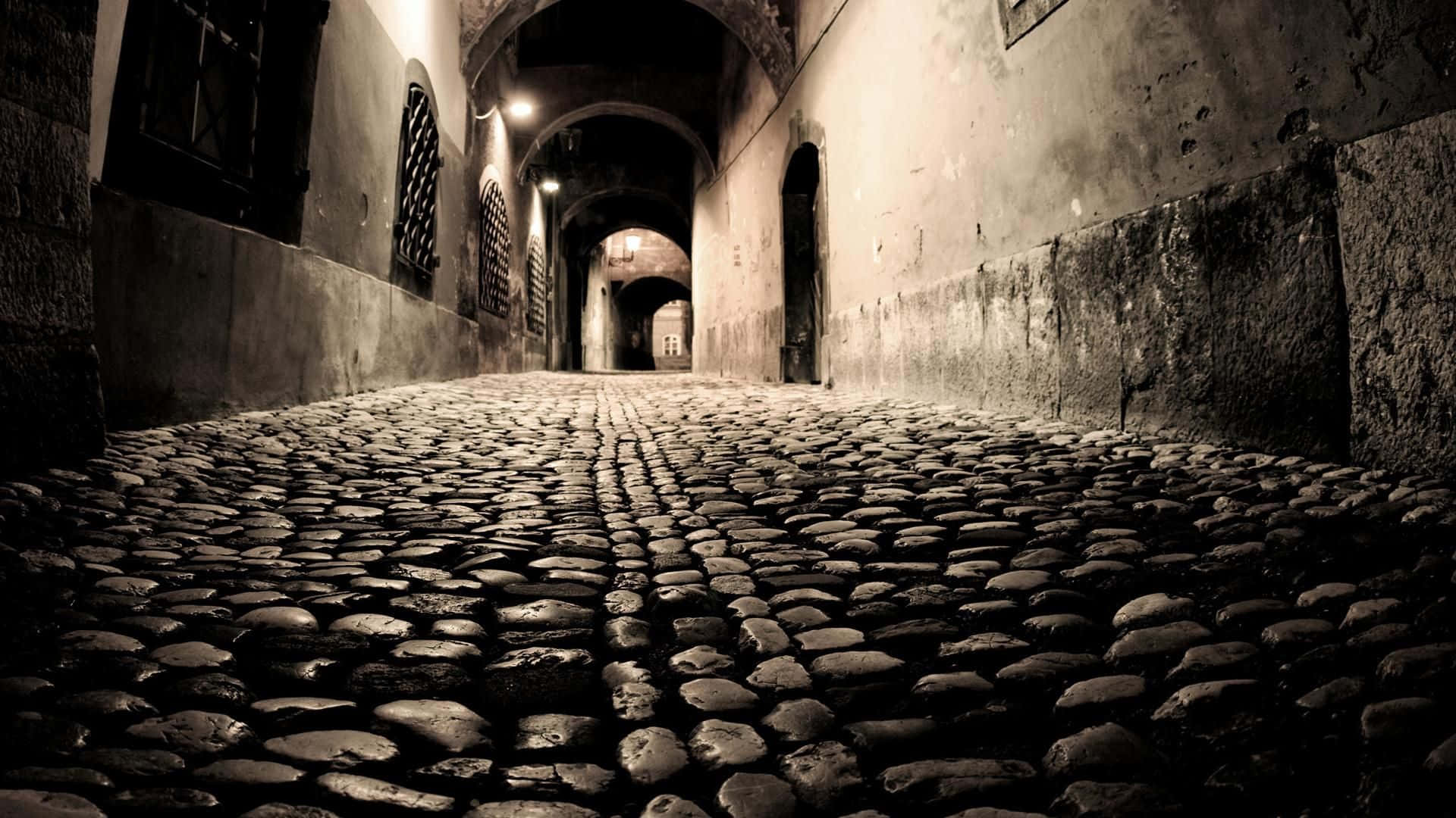 Dark Alleyway 桌布 壁紙 — 一條狹窄的鵝卵石小巷，有拱形石牆和昏暗的暖光，逐漸消失在黑暗中。