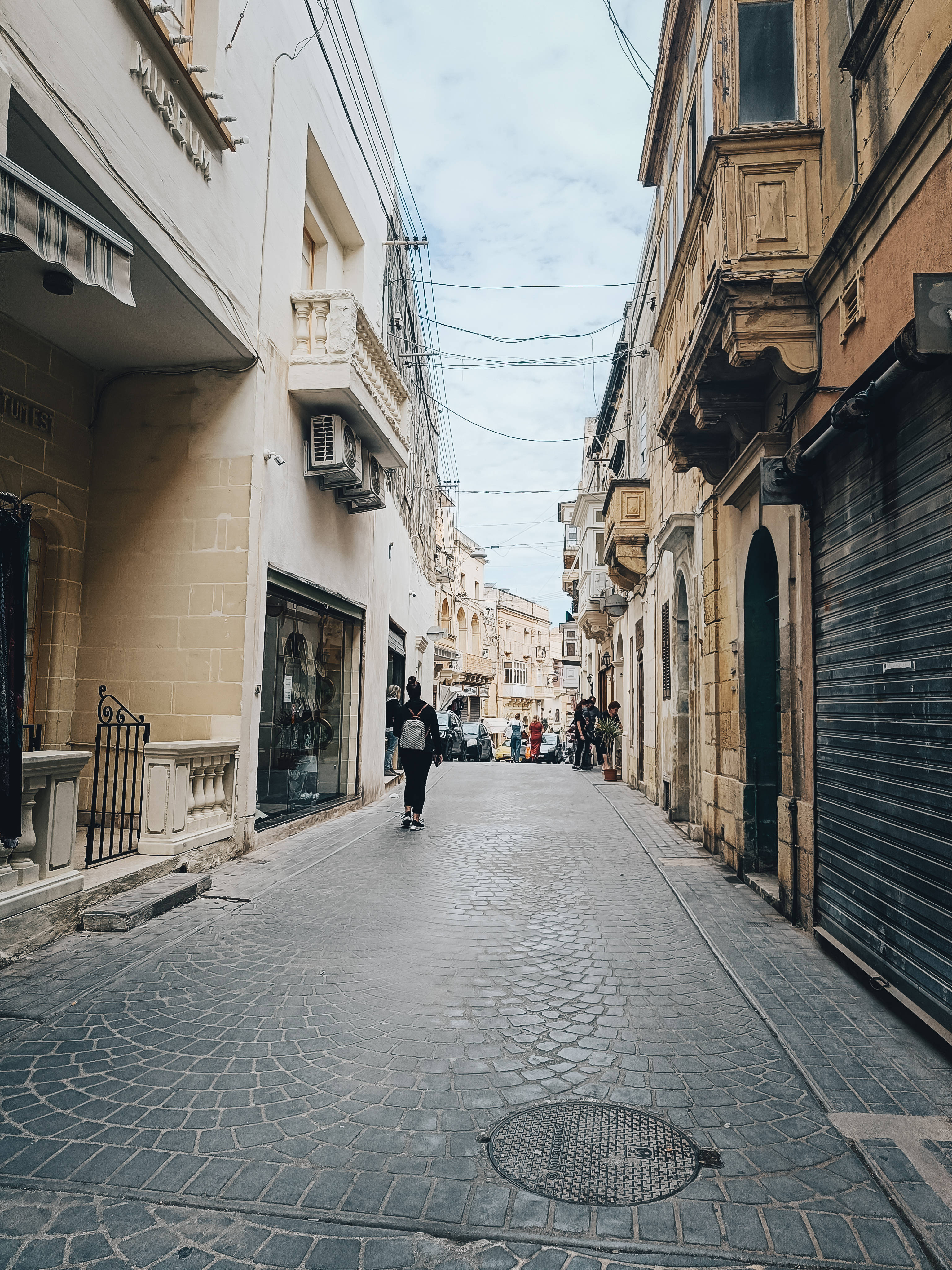 Malta 桌布 壁紙 — 一條狹窄的鵝卵石街道，位於歷史悠久的歐洲小鎮，兩旁是粉彩建築，一名孤獨的行人正走向遠處的人影。