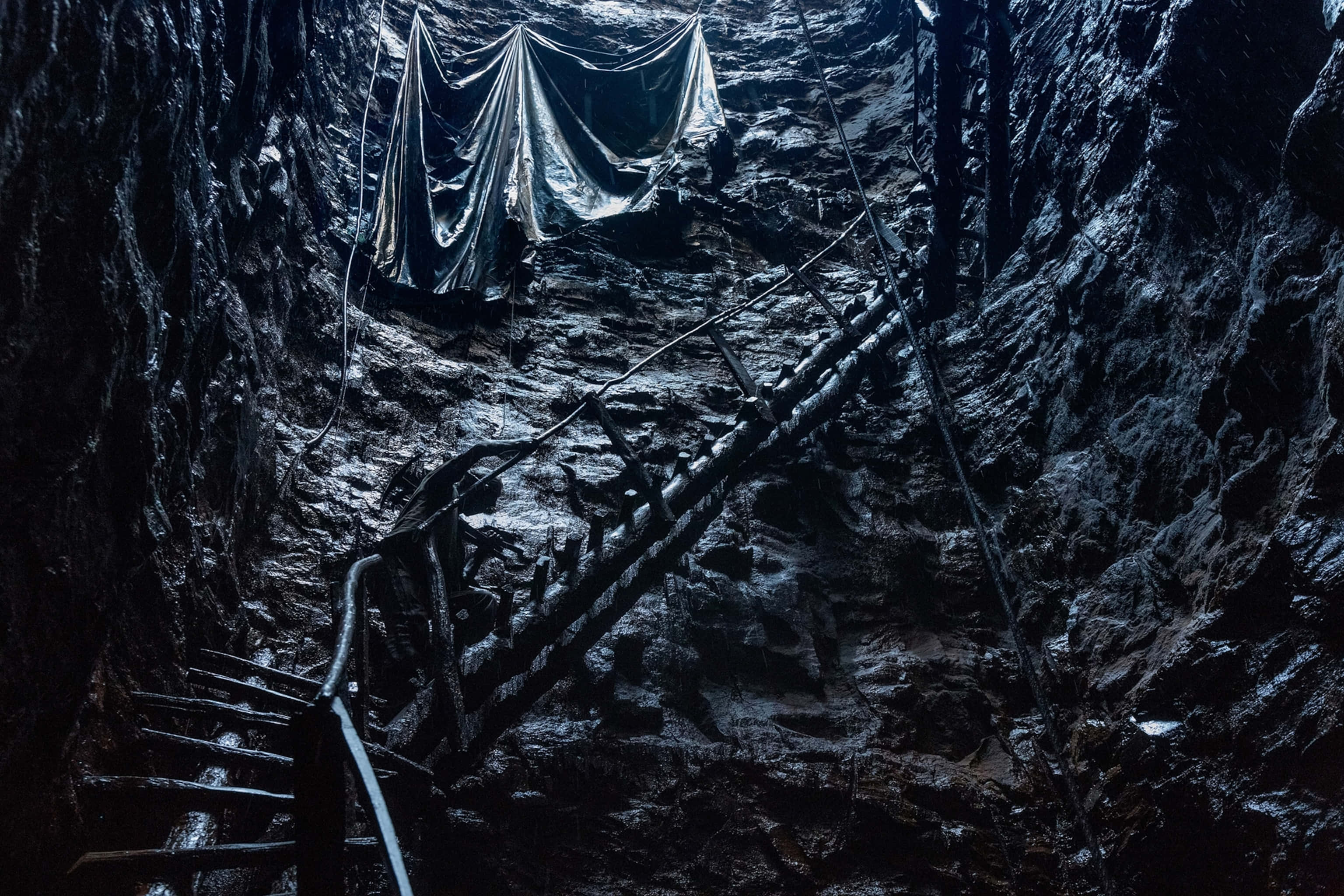 Coal Mining 桌布 壁紙 — 一條生鏽的金屬樓梯向下延伸至一個黑暗潮濕的洞穴，頭頂懸掛著破爛的塑膠布。