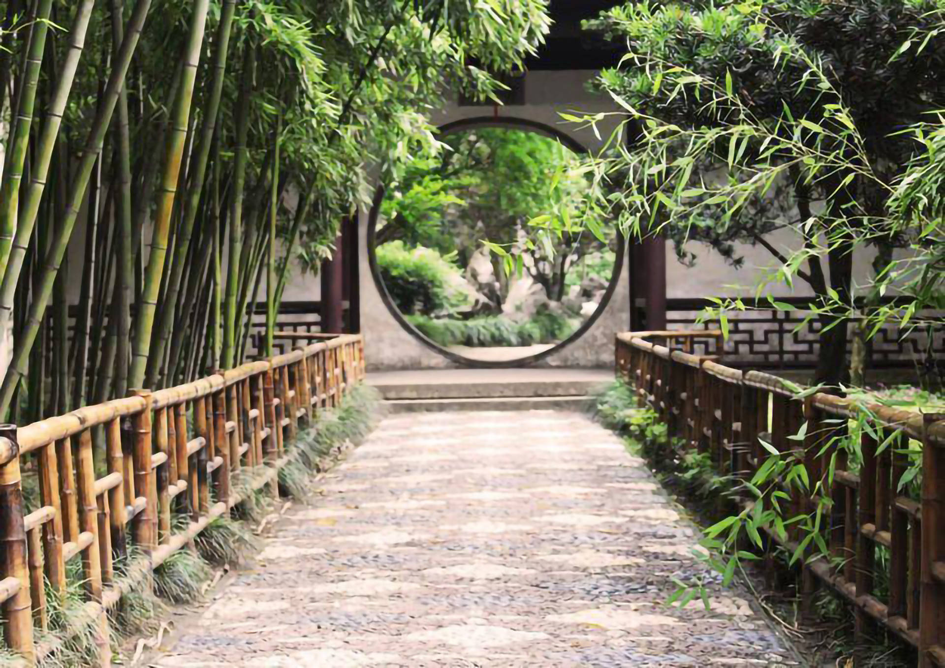 Suzhou 桌布 壁紙 — 一條由竹籬笆夾道的石徑通往圓形月門，門後展現出寧靜的花園。