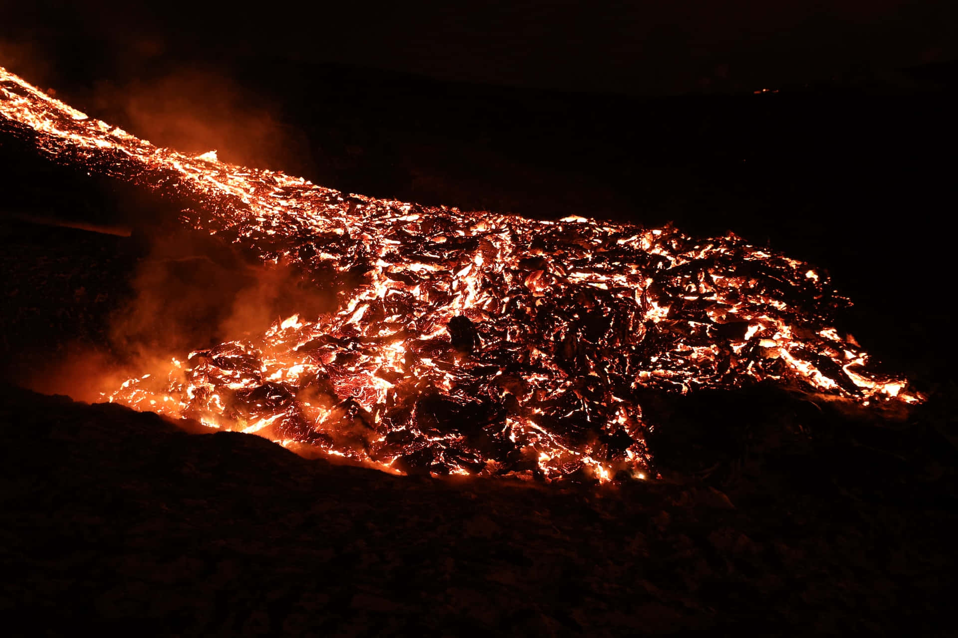Captivating 桌布 壁紙 — 一條發光的橙色熔岩河流在夜空下流過黑暗的火山景觀。