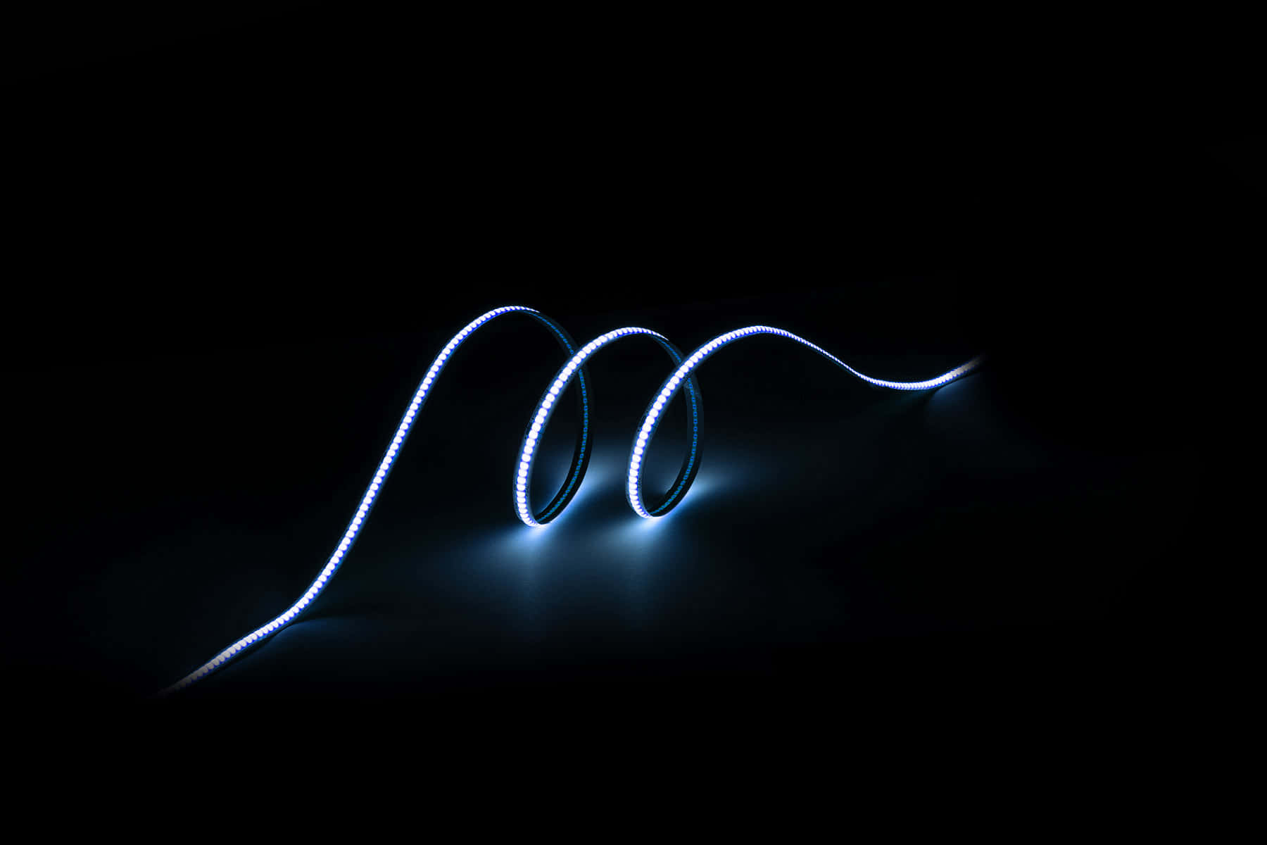 lighting 桌布 壁紙 — 一條發光的藍色LED燈帶在漆黑的背景上優雅地盤繞成曲線，散發出冷光。