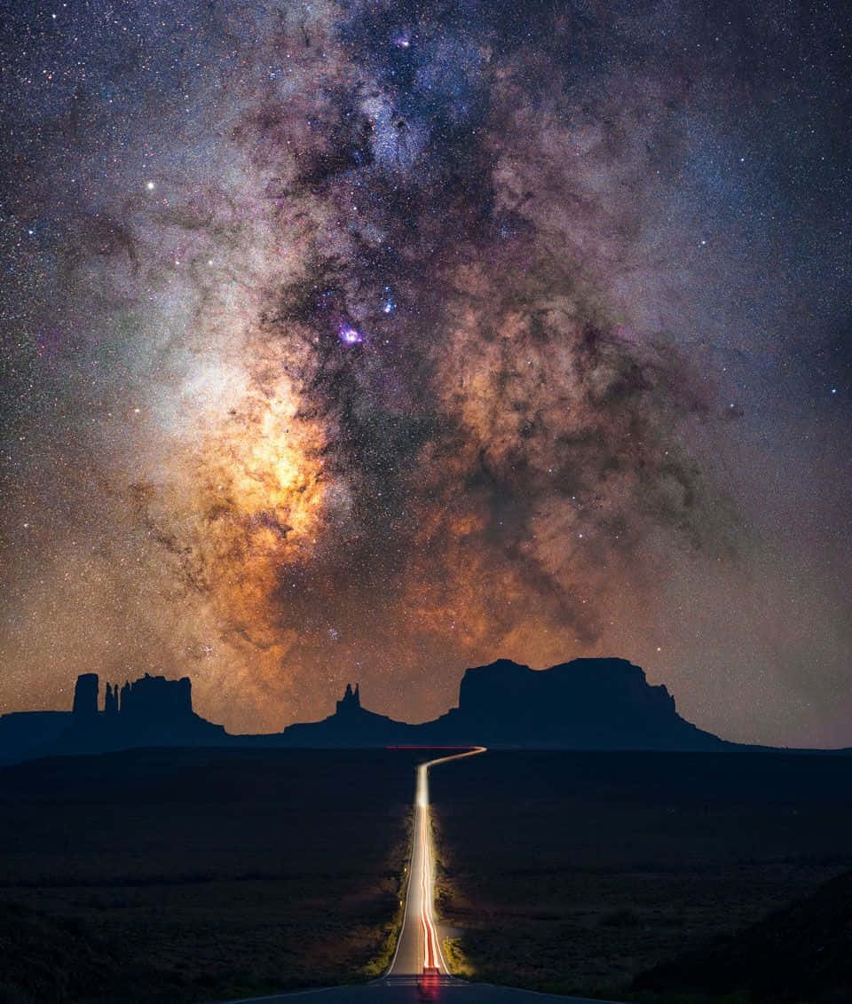 Galactic Center 桌布 壁紙 — 一條發光的道路在充滿星星和宇宙塵埃的 vibrant 銀河系下，伸向遙遠的孤峰。