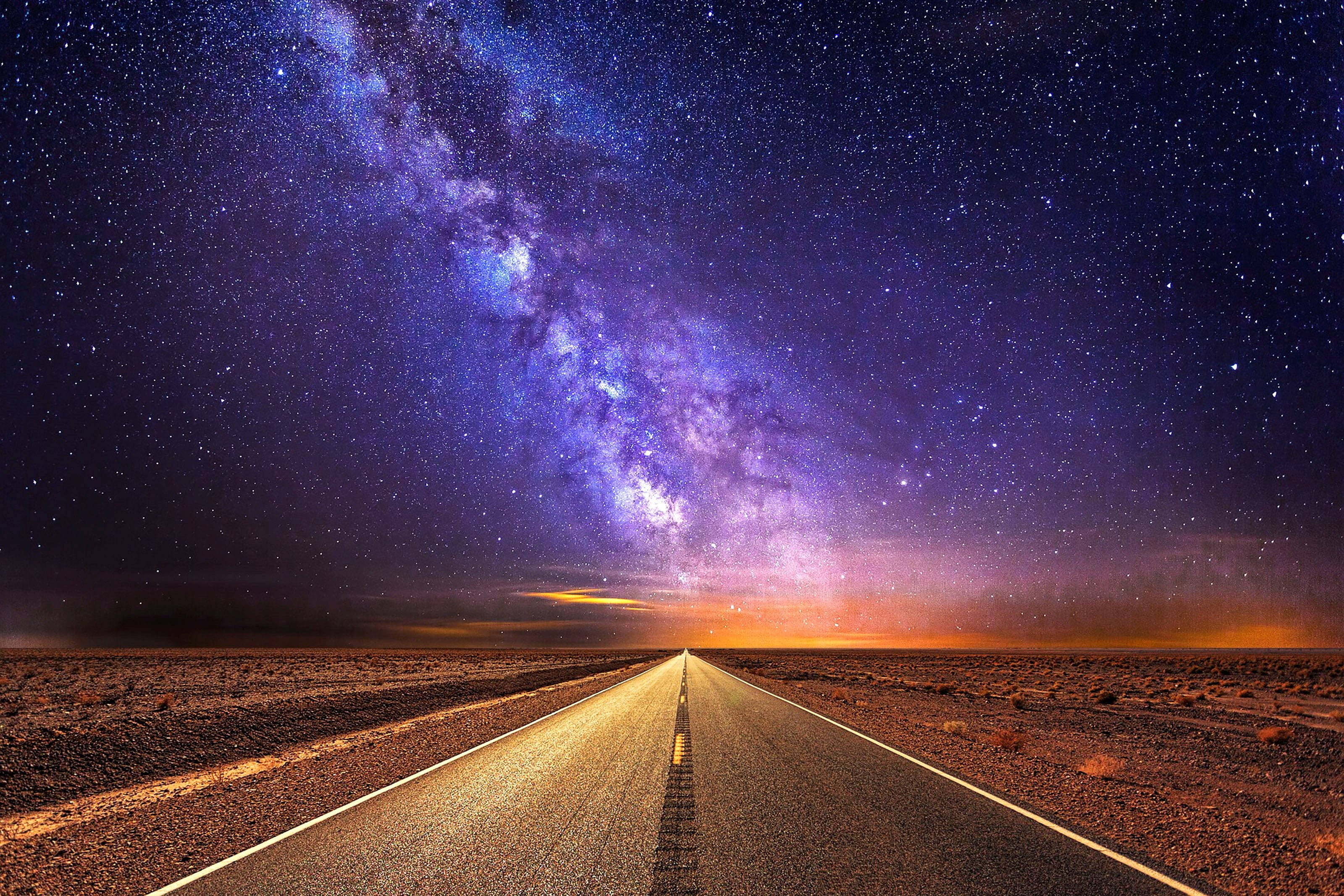 Road 桌布 壁紙 — 一條發光的道路延伸到地平線，下方是充滿銀河系的鮮豔紫色和橙色星空。
