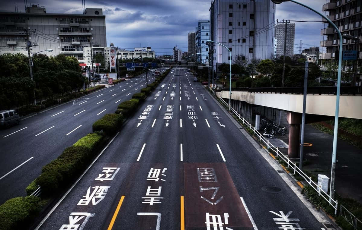 Road 桌布 壁紙 — 一條空蕩的多車道城市高速公路在陰沉多雲的天空下延伸，瀝青上繪有日文字元。