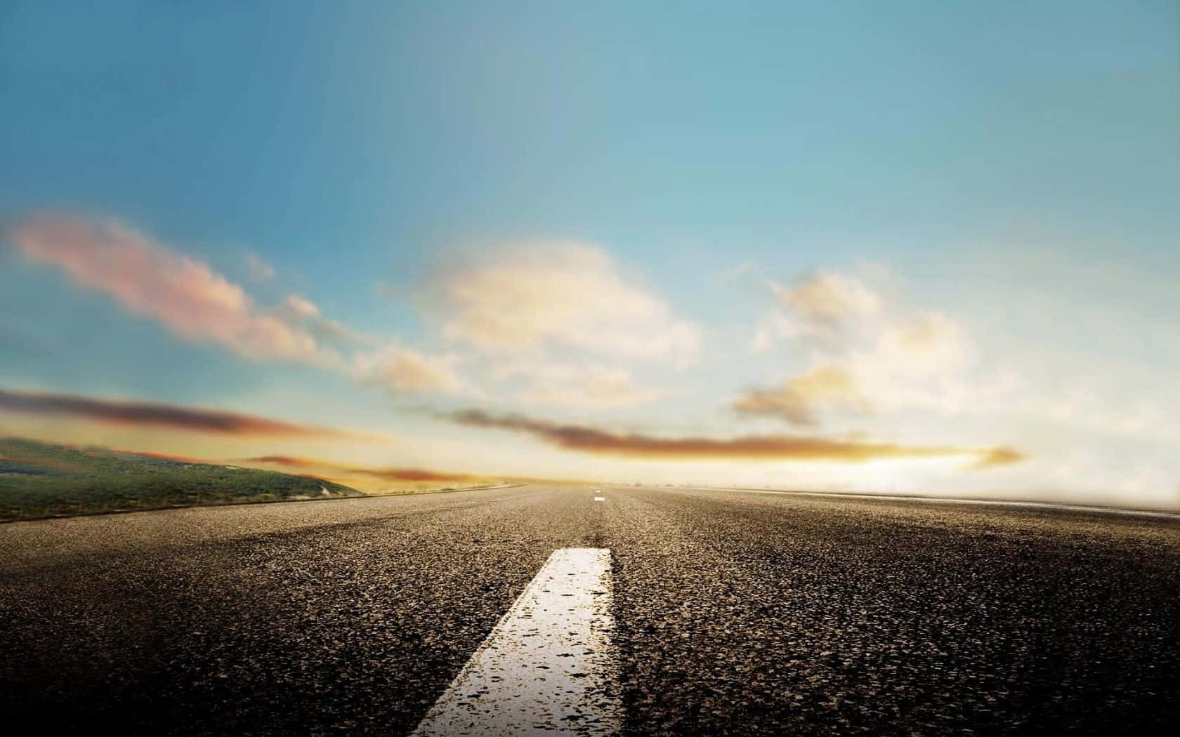 Road 桌布 壁紙 — 一條空蕩蕩的瀝青路延伸向金色的日落，天空清澈湛藍，散落著雲朵和遠山。