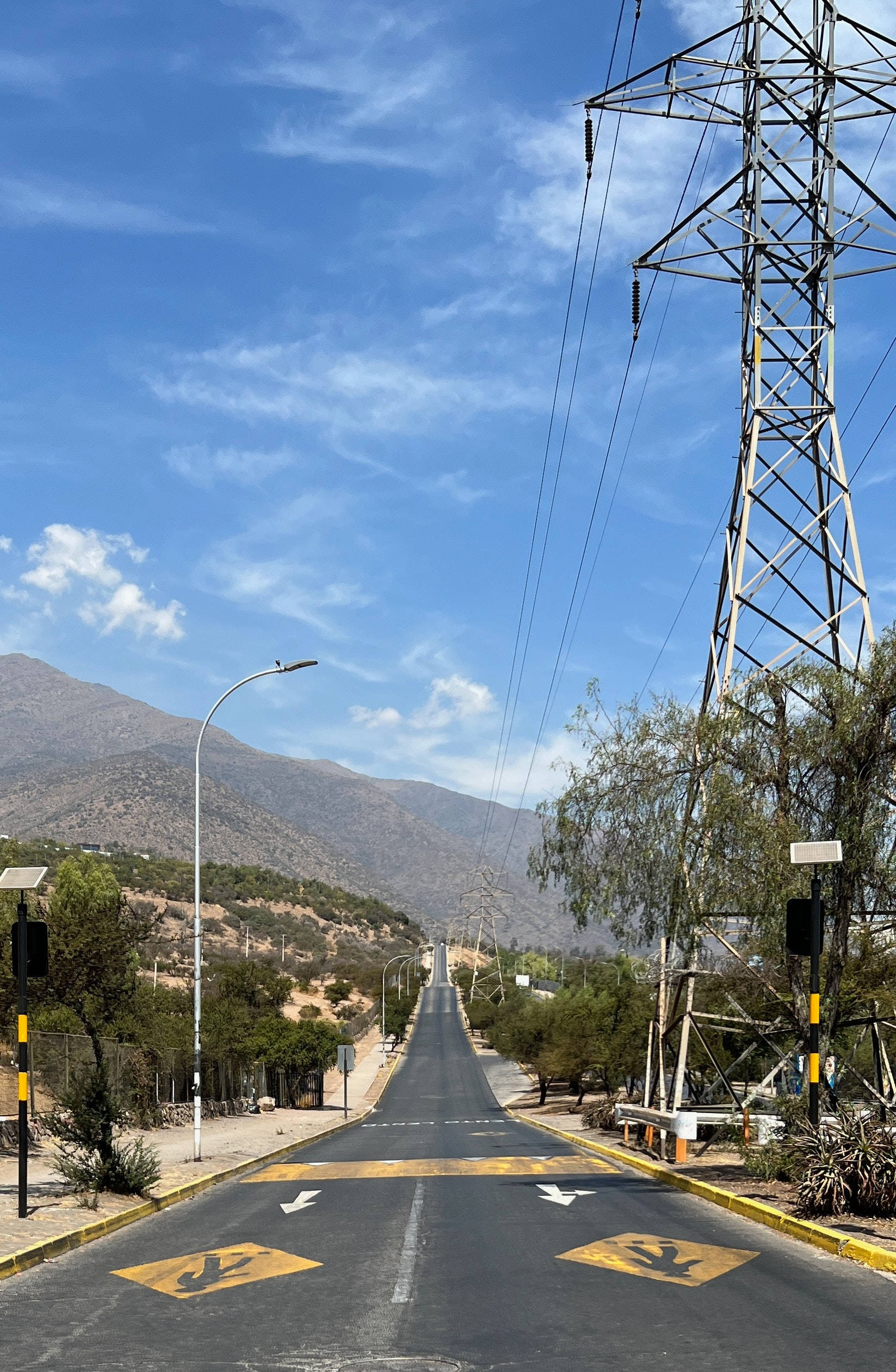 Road 桌布 壁紙 — 一條筆直的柏油路在明亮藍天和薄雲下延伸至遠山，右側有一座高壓電塔。