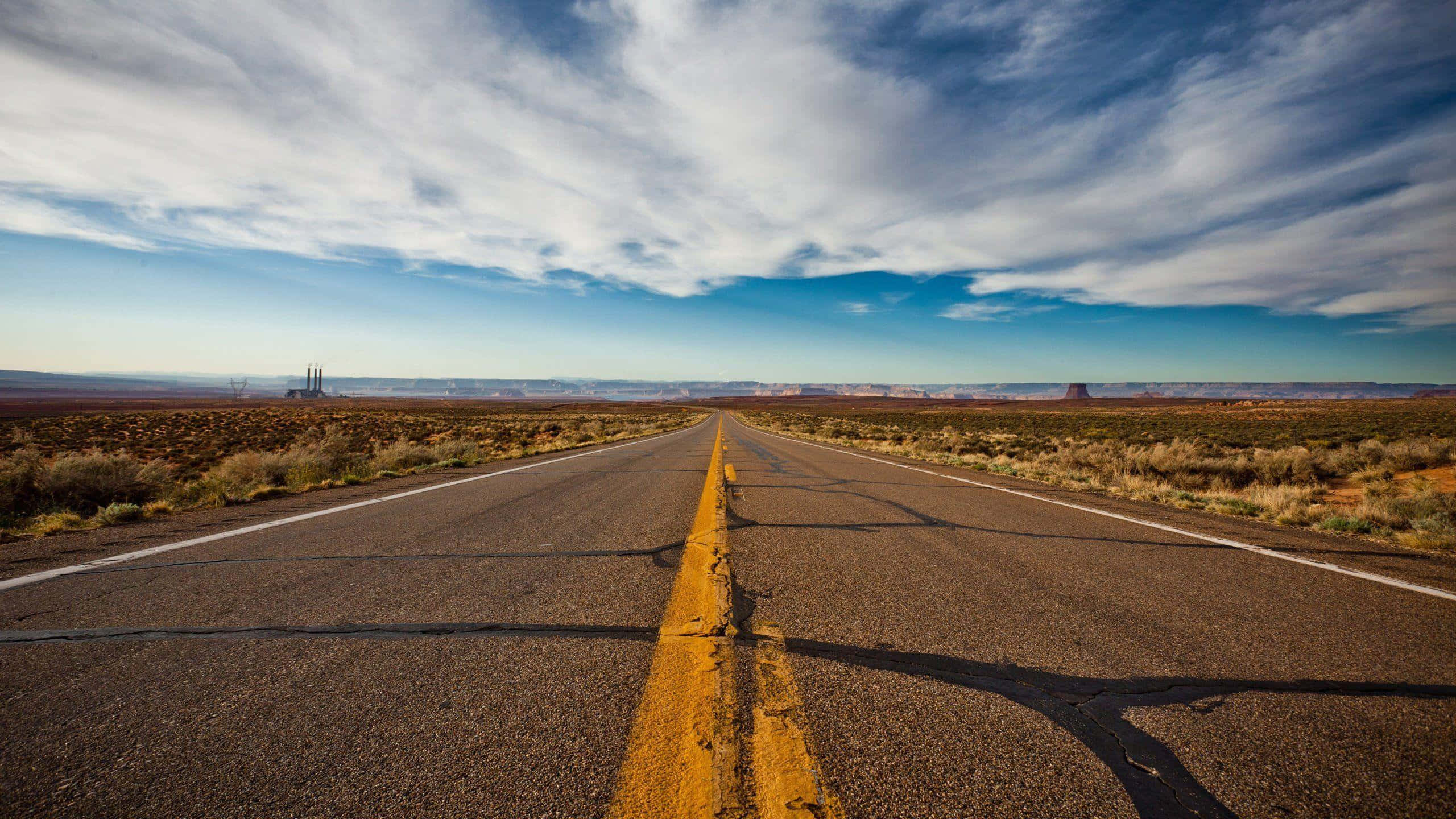 Highways 桌布 壁紙 — 一條筆直的沙漠高速公路在廣闊的天空下延伸向遠處的平頂山，天空中有縷縷雲彩。