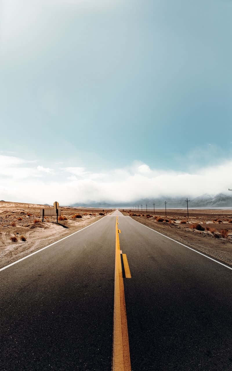 加州 桌布 壁紙 — 一條筆直的瀝青公路穿過荒蕪的沙漠景觀，延伸至遠方，天空廣闊湛藍，遠處群山連綿。