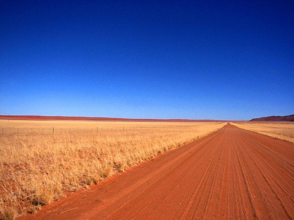 Namibia 桌布 壁紙 — 一條筆直的紅土路在廣闊清澈的藍天下無盡地延伸穿過金色的草原。
