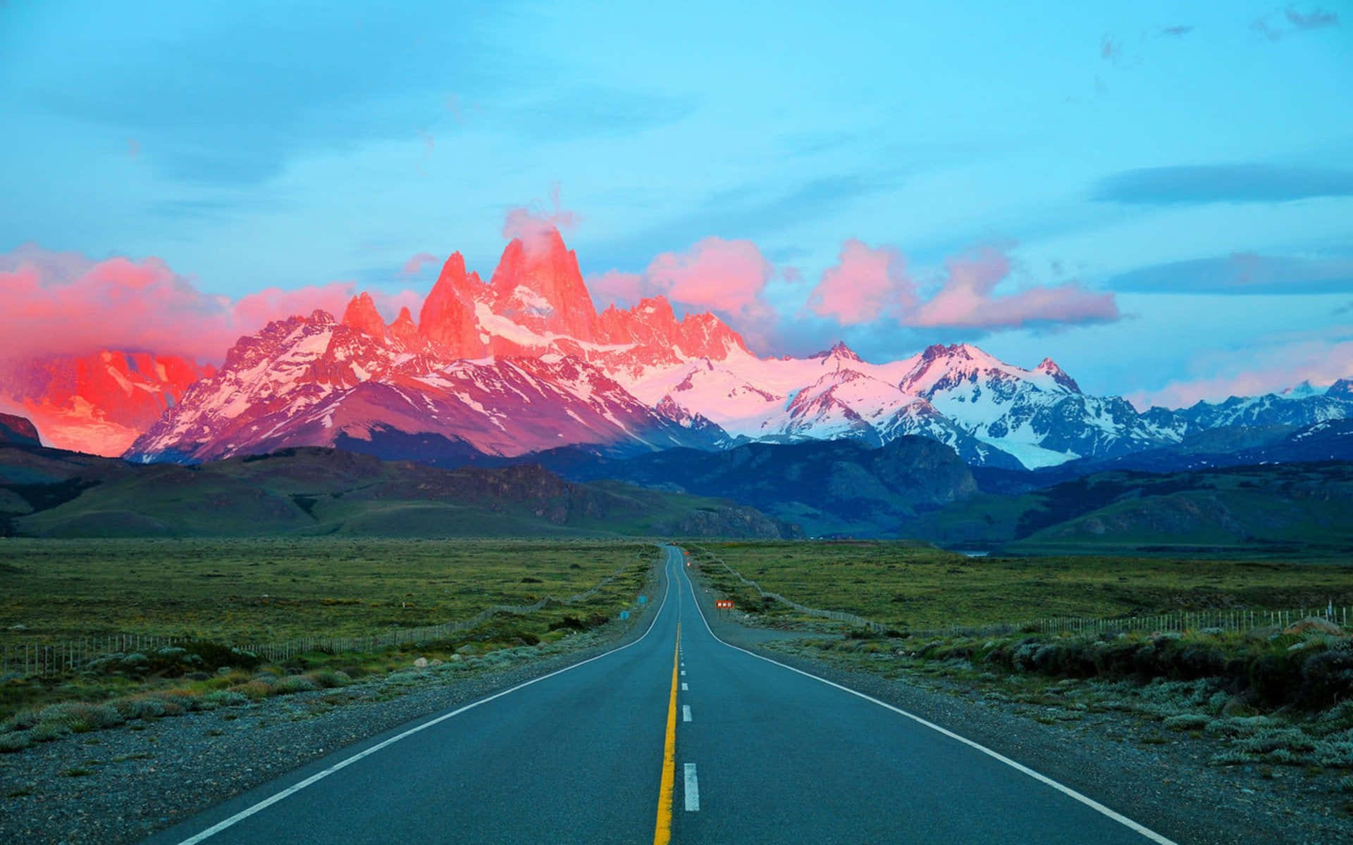 Patagonia 桌布 壁紙 — 一條筆直的道路延伸向日落時分閃耀著粉紅色和橙色的雪山。