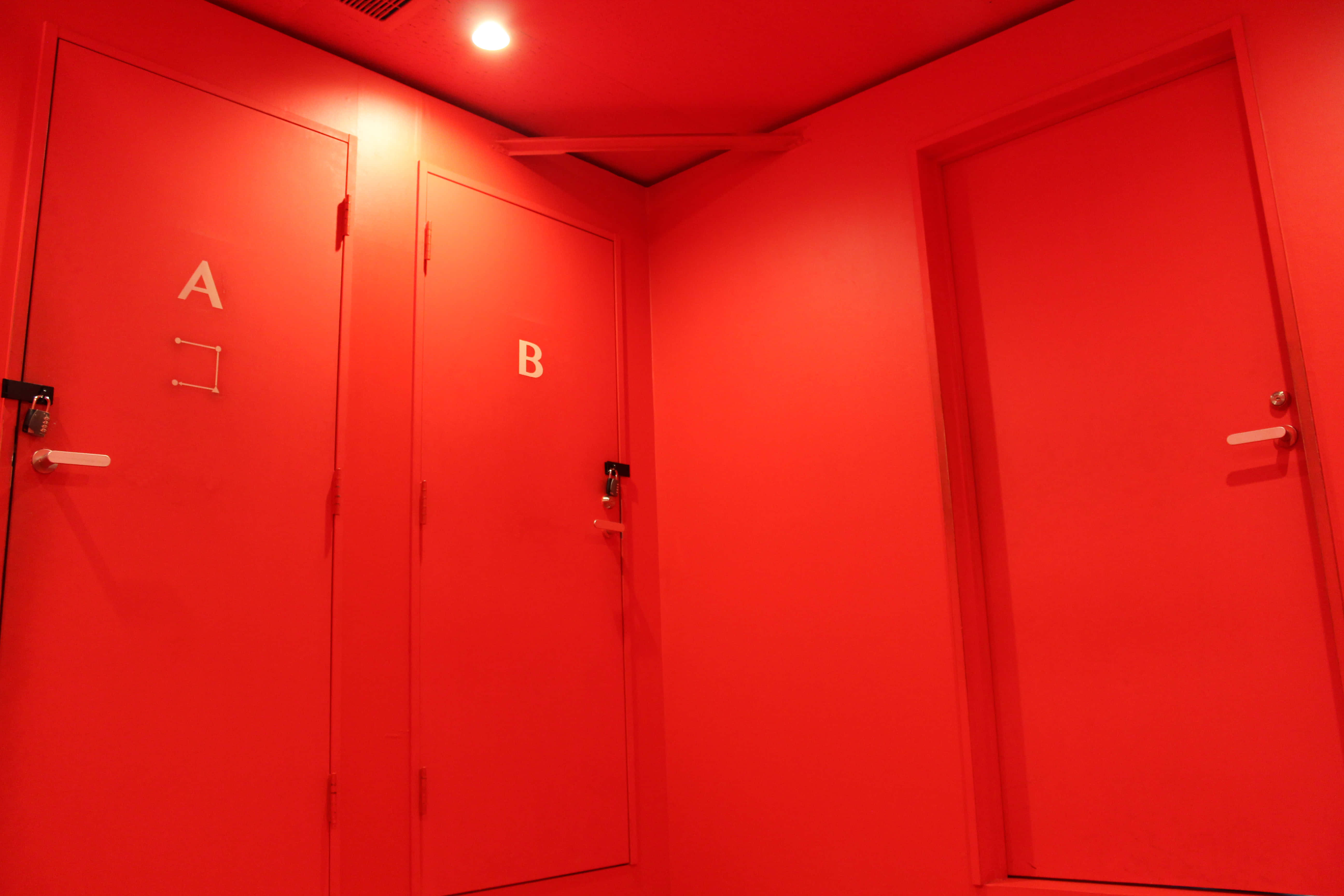Red Room 桌布 壁紙 — 一條簡潔的紅色走廊，有三扇門標有 A B，還有一扇未標記的門在單一天花板燈下發光。