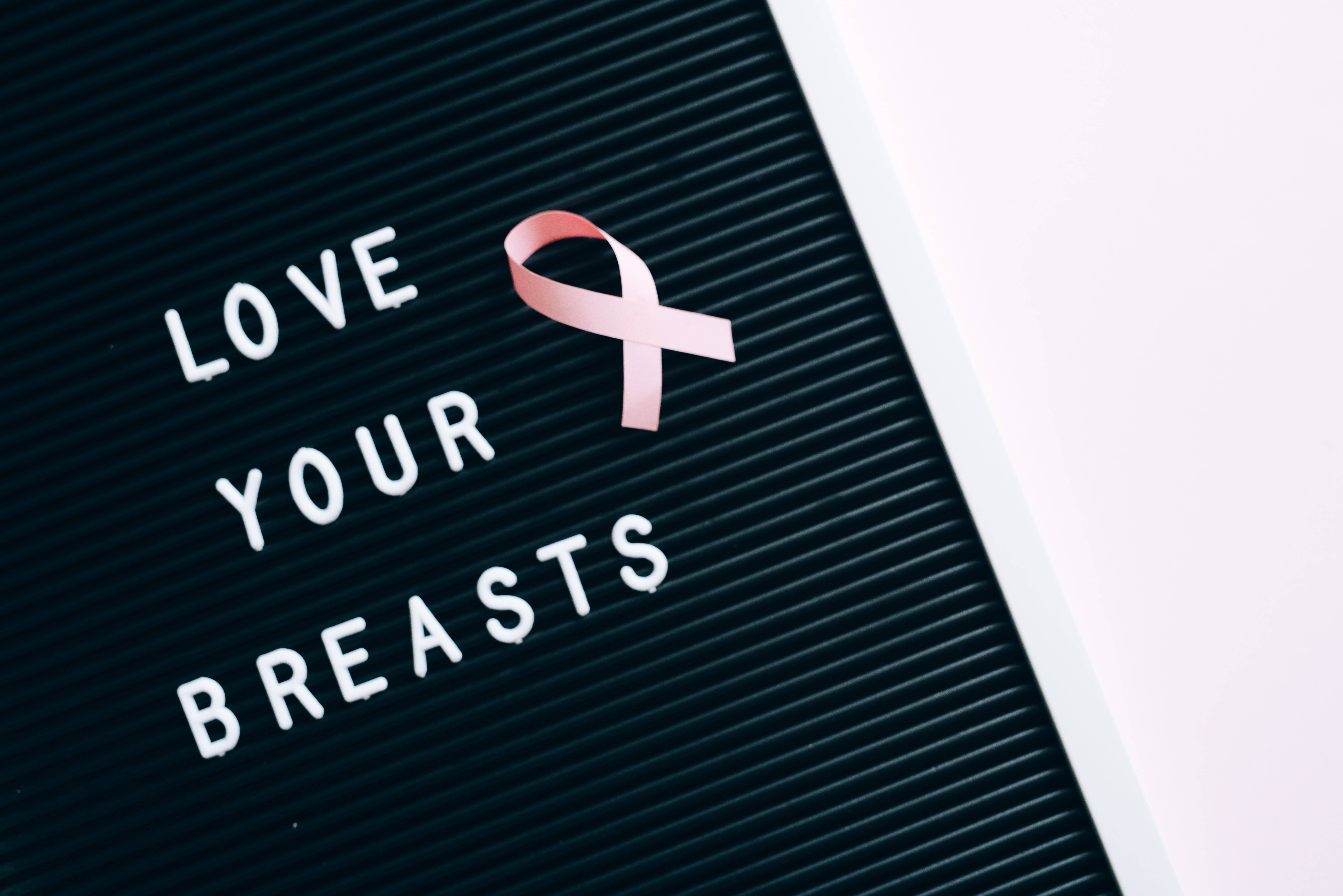Breast Cancer Awareness 桌布 壁紙 — 一條粉紅色乳癌意識絲帶放在黑色字母板上，旁邊寫著「LOVE YOUR BREASTS」。