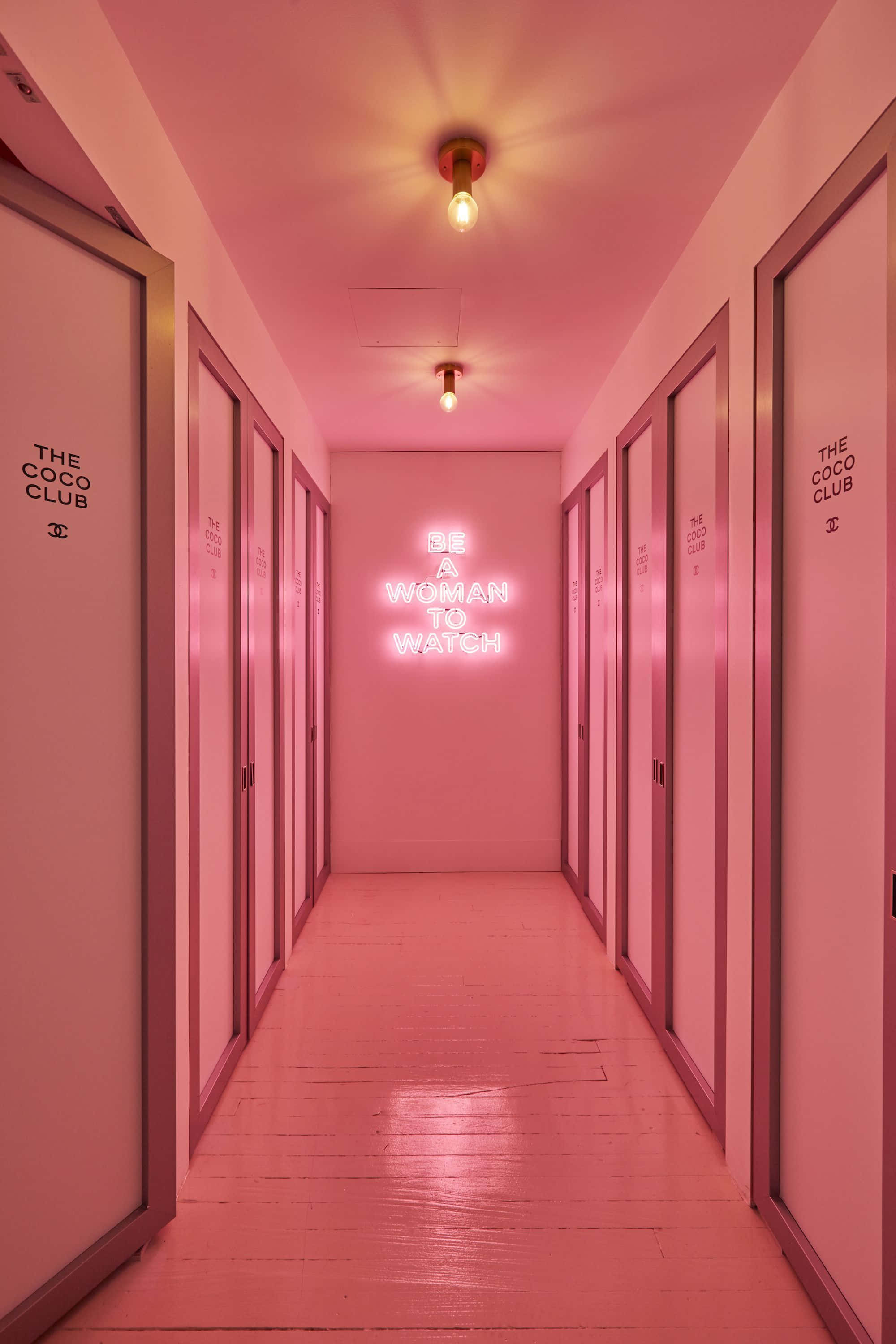 Boujee Aesthetic 桌布 壁紙 — 一條粉紅色燈光的走廊，門上標有「THE COCO CLUB」，盡頭有一個霓虹燈牌寫著「BE A WOMAN TO WATCH」。