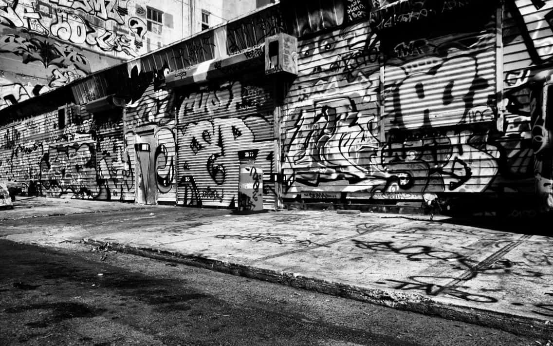 Black And White Street 桌布 壁紙 — 一條粗糙的黑白城市小巷，波浪形金屬百葉窗和路面上覆蓋著密集的塗鴉。