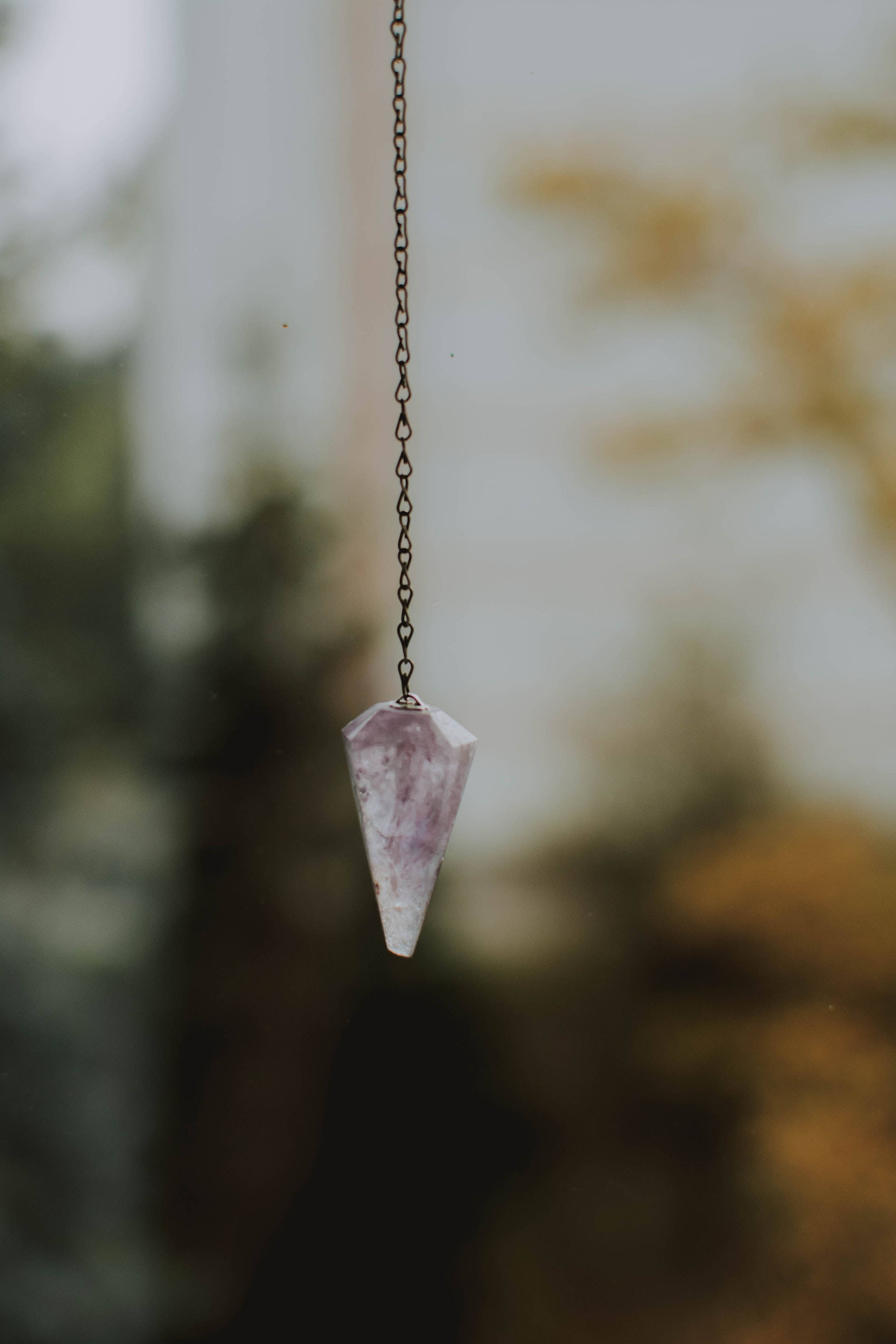 紫水晶 桌布 壁紙 — 一條精緻的紫色紫水晶吊墜懸掛在鏈條上，背景是柔和模糊的自然景色。