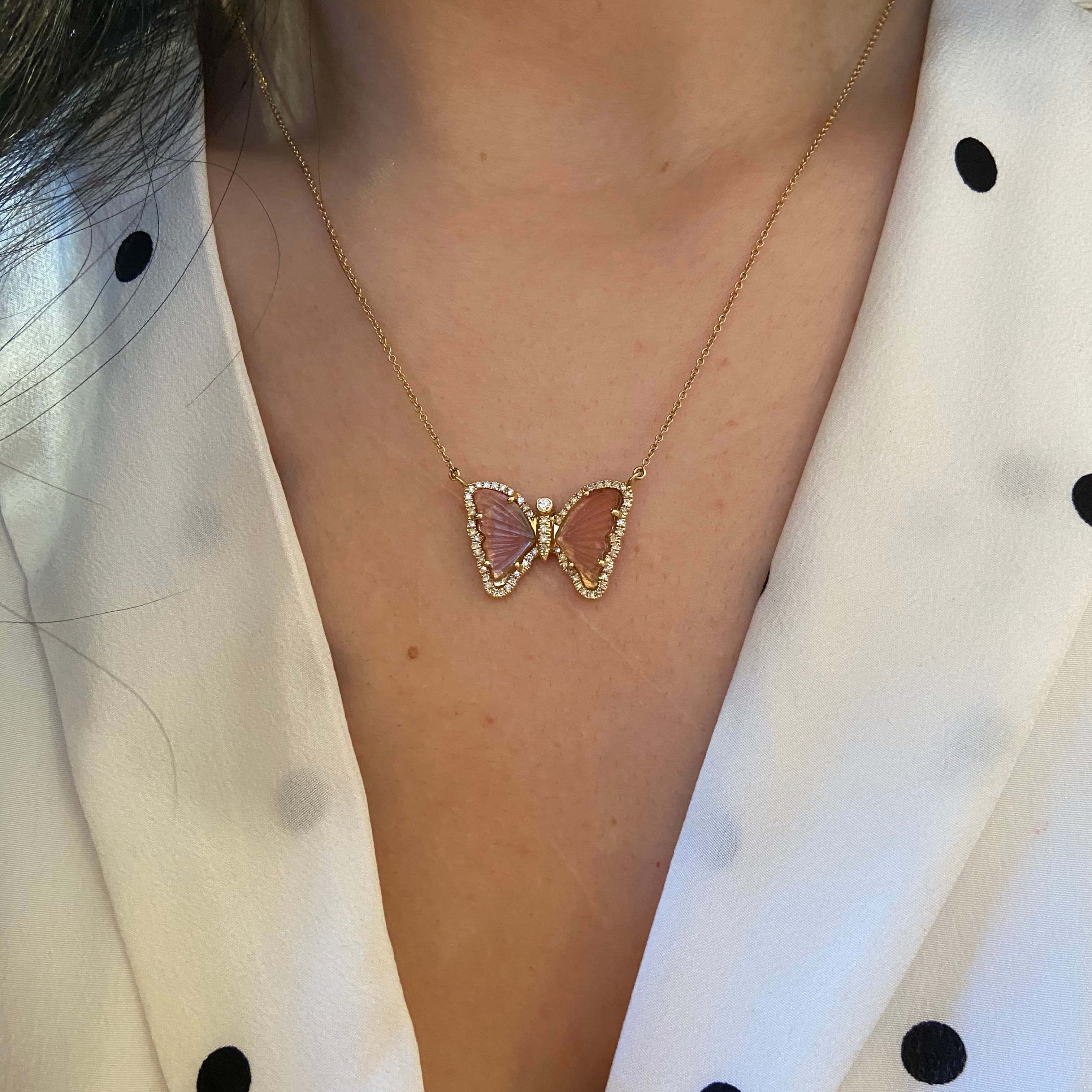 Butterfly Jewelry 桌布 壁紙 — 一條精緻的金色蝴蝶項鍊，帶有粉紅色寶石翅膀，放在一位穿著白色圓點襯衫的人身上。