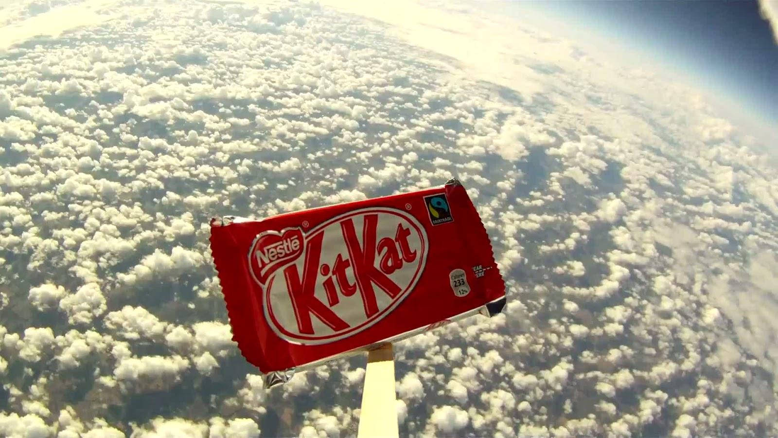 Chocolate 桌布 壁紙 — 一條紅色KitKat在彎曲的藍色地球上，漂浮在蓬鬆的白雲之上。