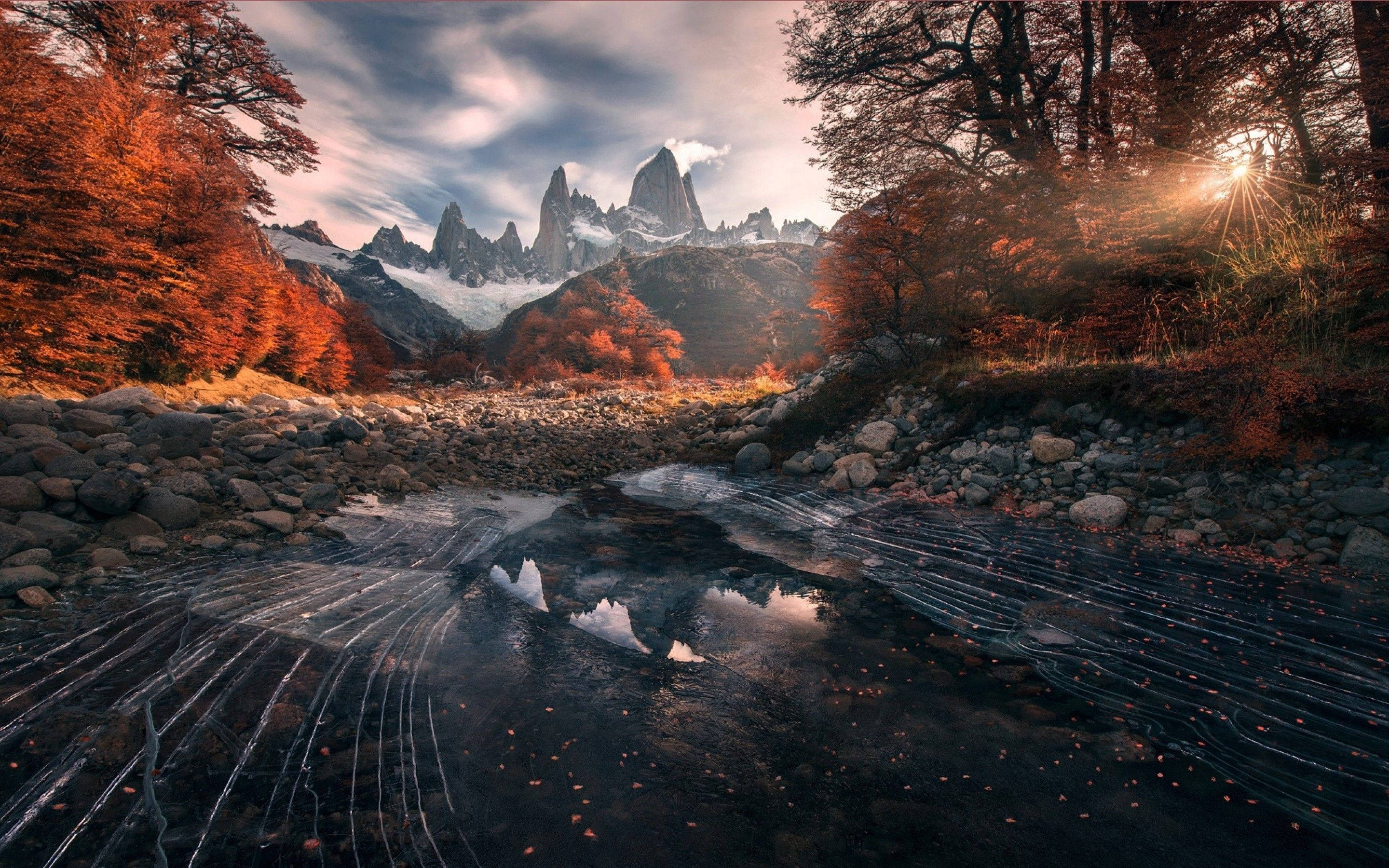 Patagonia 桌布 壁紙 — 一條結冰的小溪在戲劇性的日出天空下，倒映著白雪覆蓋的山峰和火紅的秋樹。