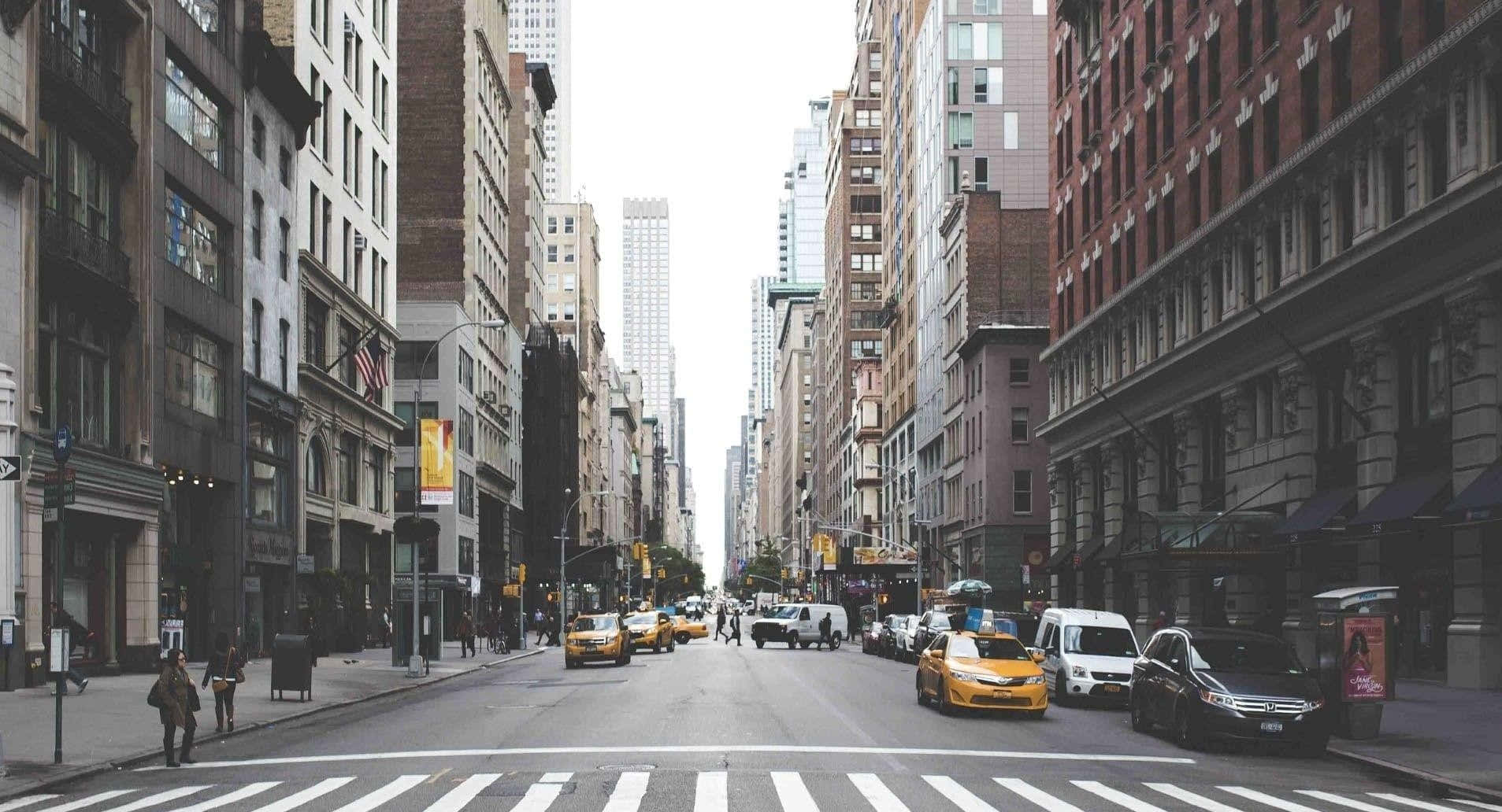 New York 桌布 壁紙 — 一條繁忙的城市街道，兩旁高樓大廈林立，黃色計程車在陰天下行駛。