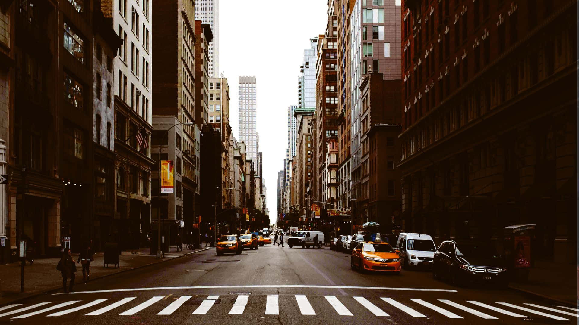 Old New York City 桌布 壁紙 — 一條繁忙的城市街道，兩旁高樓大廈林立，黃色的士和行人正在斑馬線上過馬路，天空朦朧。