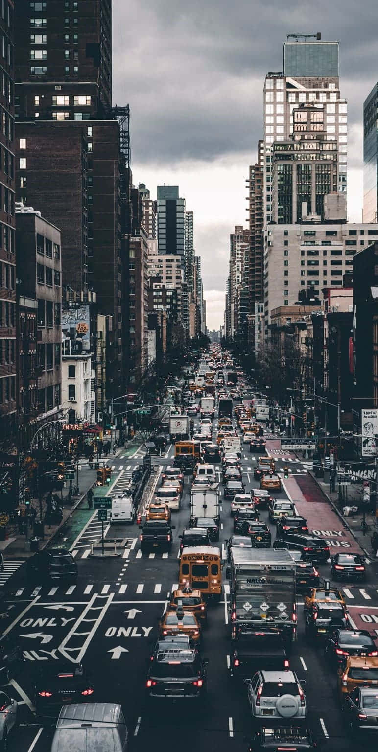 New York 桌布 壁紙 — 一條繁忙的城市街道，在沉重的灰色天空下，兩旁是高聳的摩天大樓，交通堵塞。