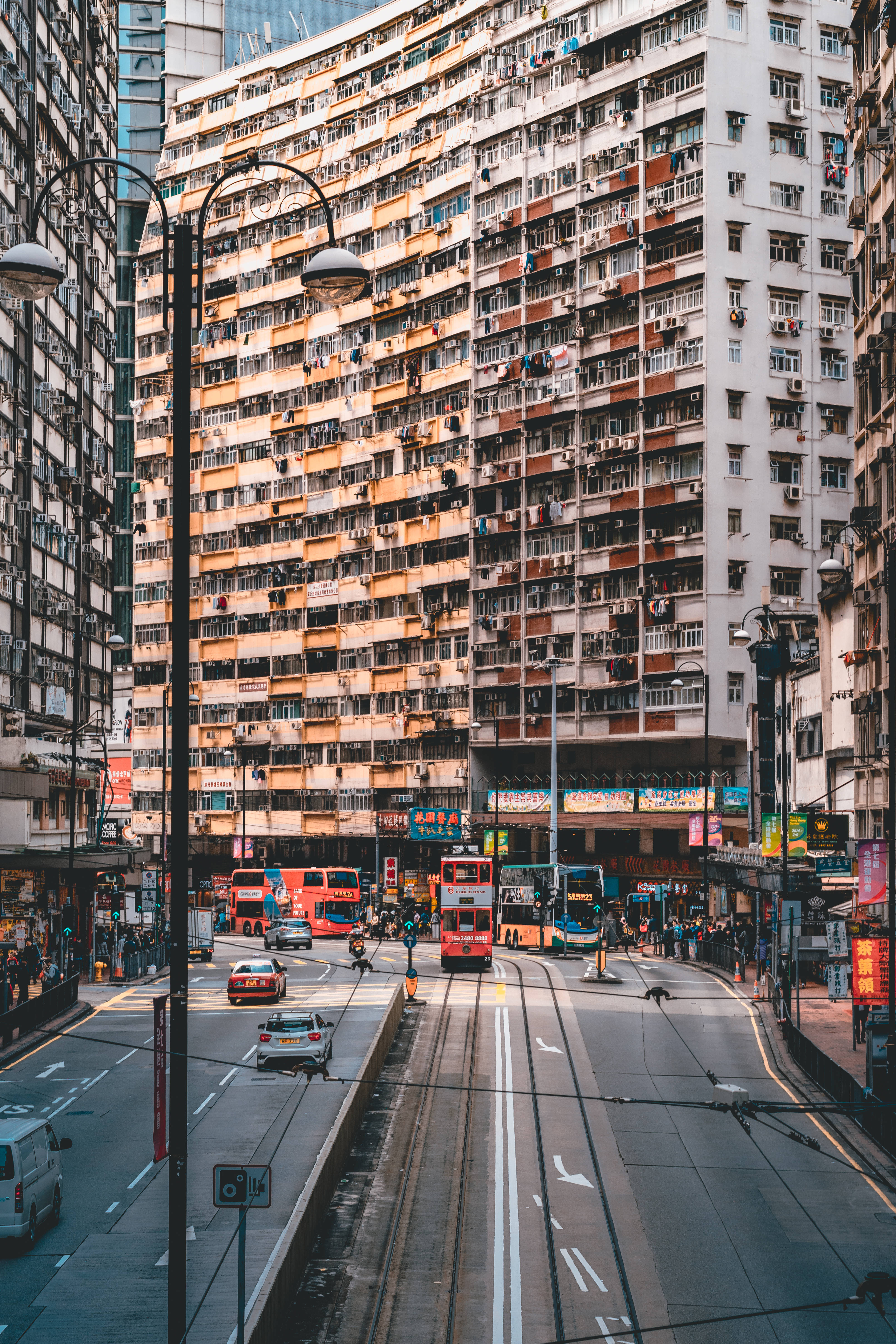 香港 桌布 壁紙 — 一條繁忙的香港街道，有紅色雙層電車和高聳的公寓大樓，佈滿陽台和空調。