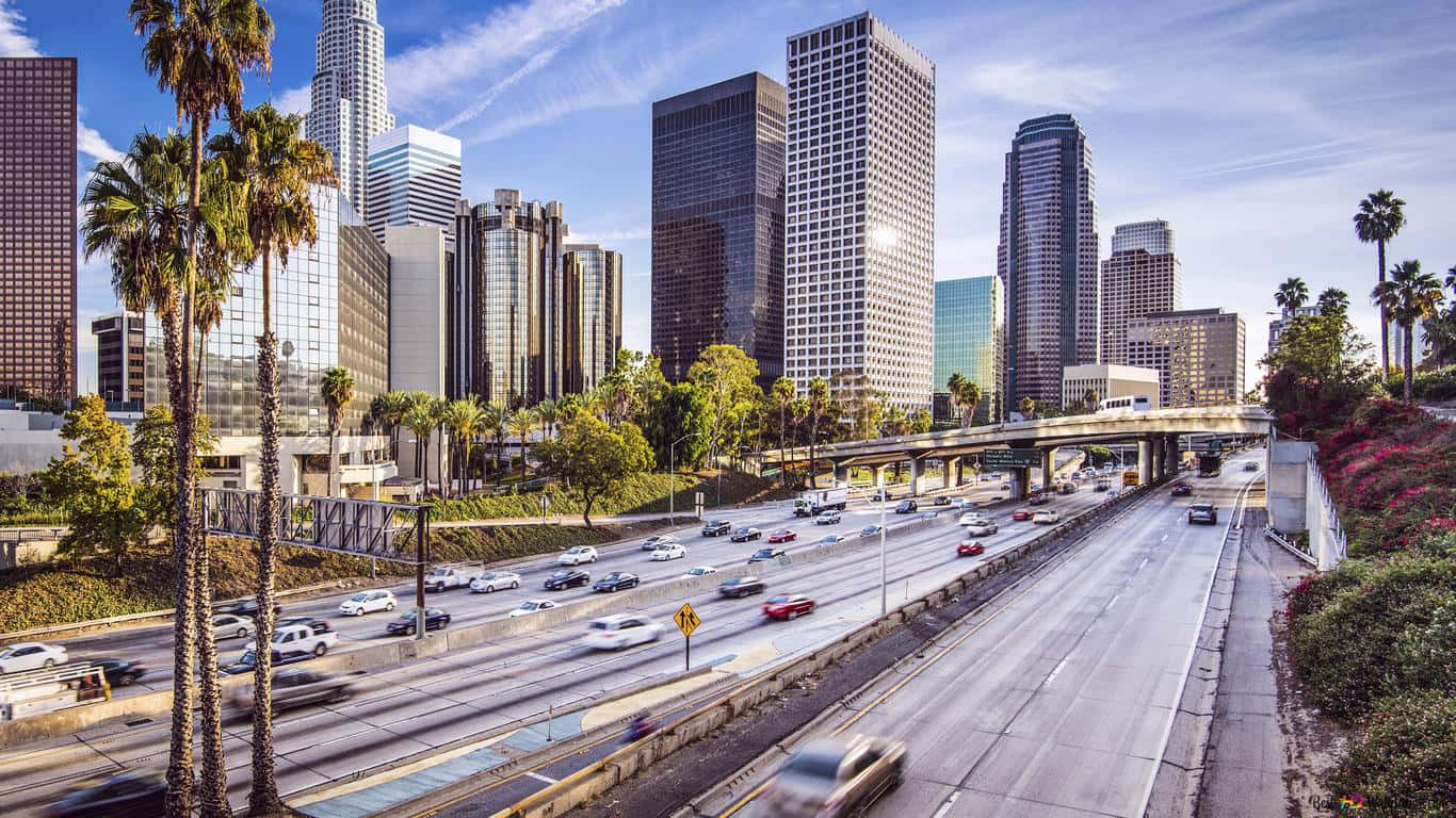 Southern California 桌布 壁紙 — 一條繁忙的高速公路穿過現代城市景觀，高聳的摩天大樓和棕櫚樹在清澈的藍天下。