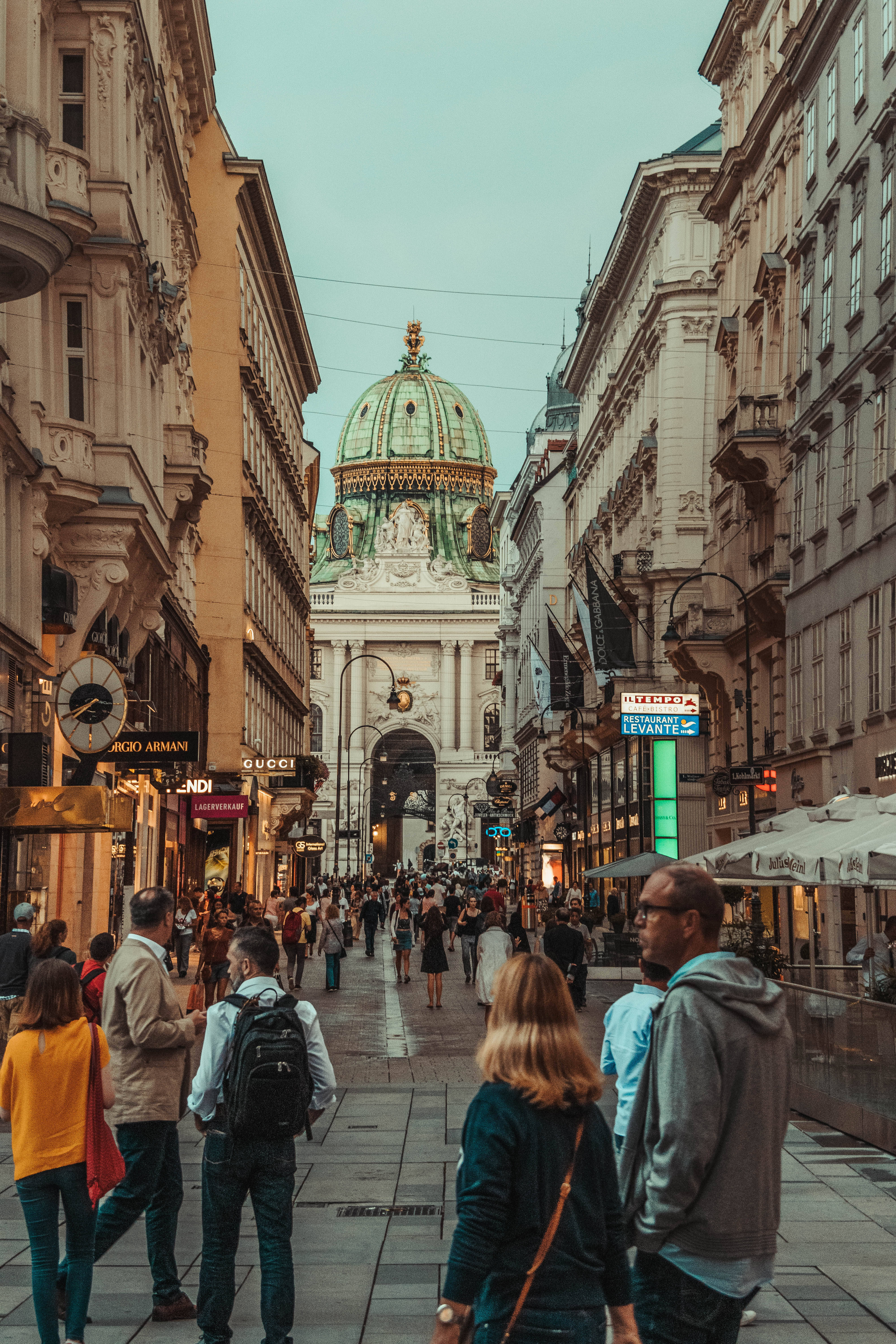 Austria 桌布 壁紙 — 一條繁華的歐洲步行街，兩旁是華麗的建築，通向一個巨大的圓頂拱門，在柔和的暮色天空下。