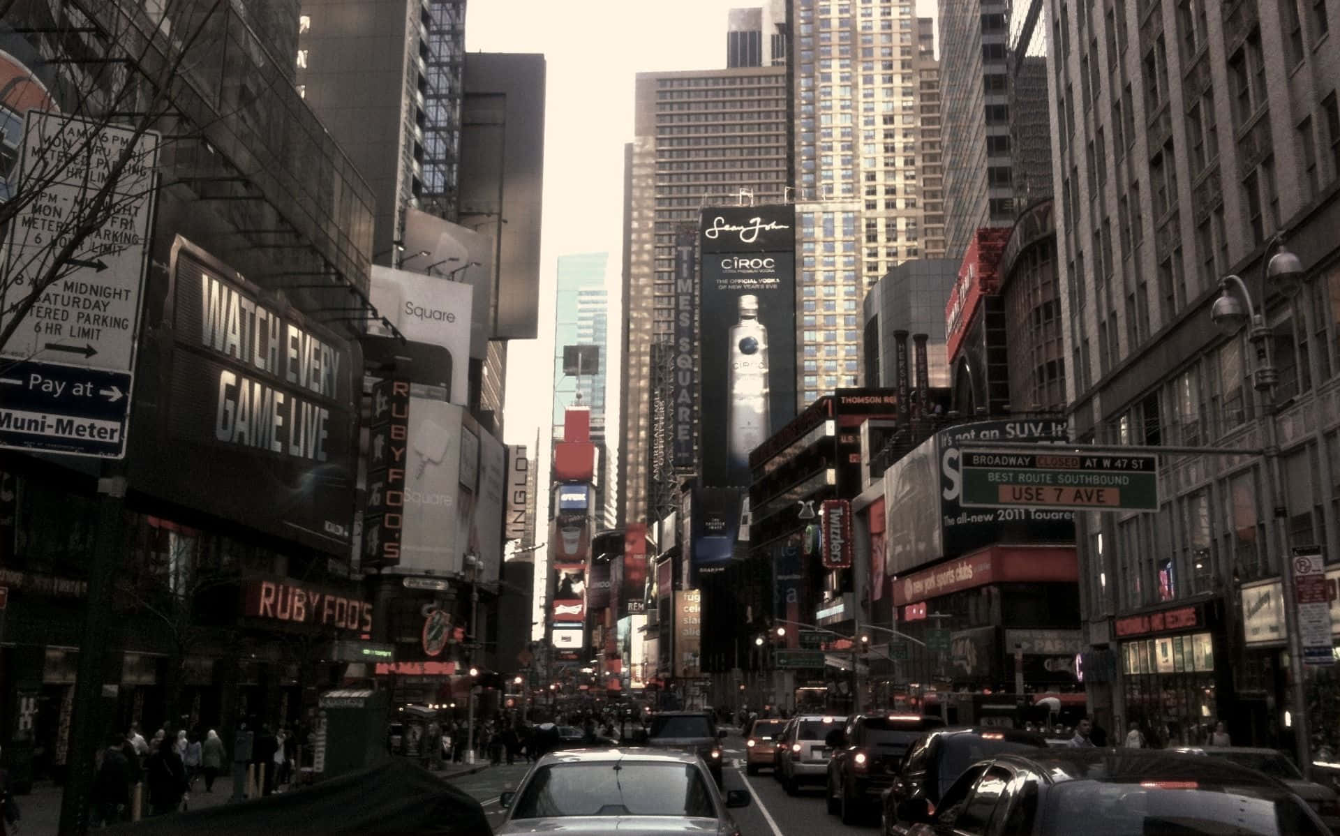 New York City Desktop 桌布 壁紙 — 一條繁華的紐約市街道，充滿高聳的摩天大樓、發光的廣告看板以及密集的車流，天空朦朧。