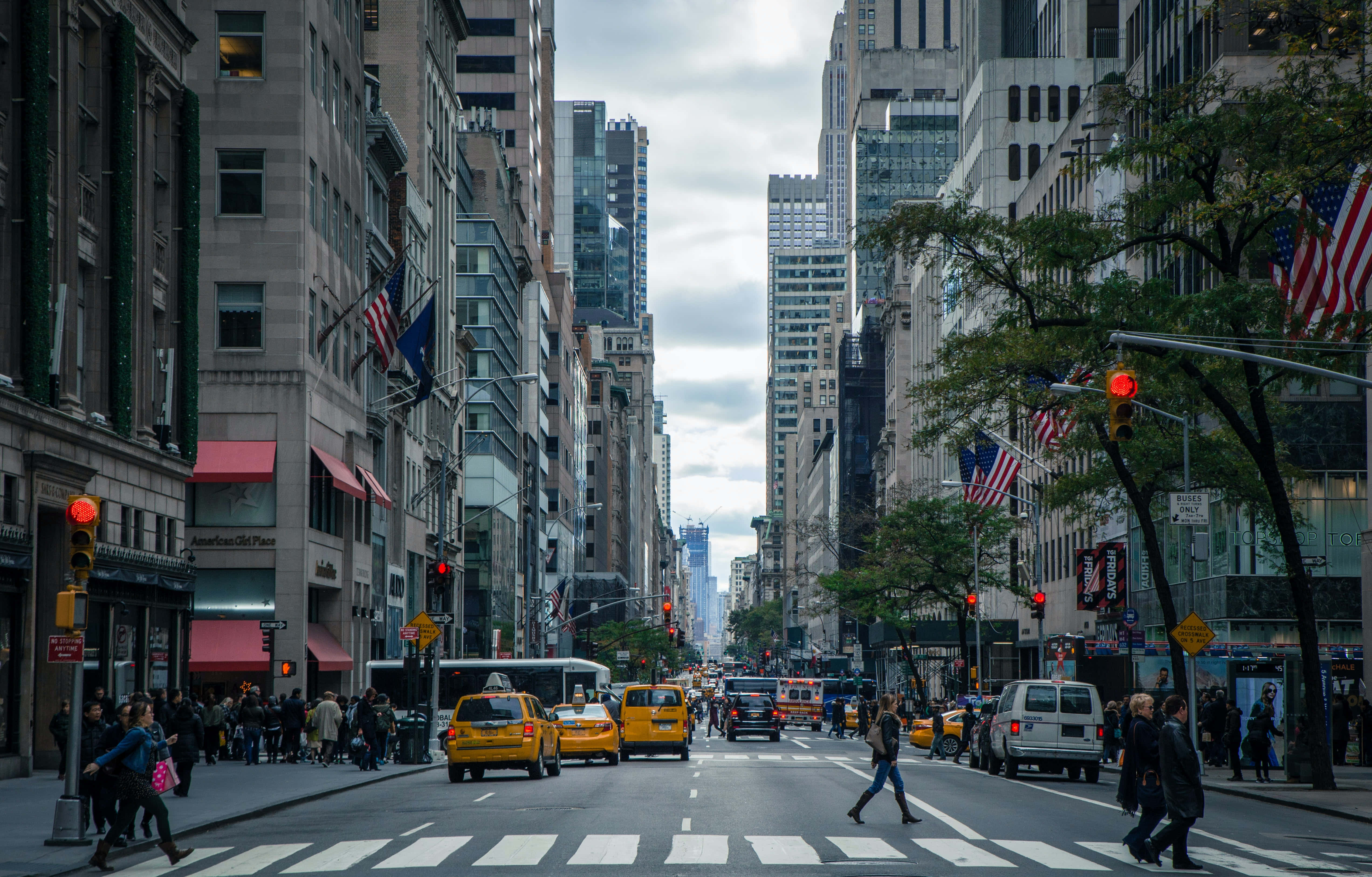 Nyc 桌布 壁紙 — 一條繁華的紐約市街道，兩旁高聳的摩天大樓林立，黃色的士和行人在陰天的人行穿越道上過馬路。