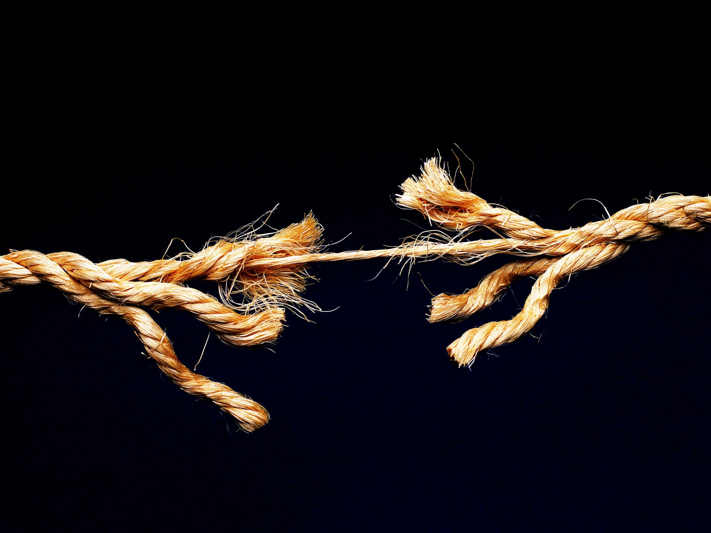 rope 桌布 壁紙 — 一條繃緊磨損的繩索在純黑背景前斷成兩半，露出粗糙的纖維和張力。