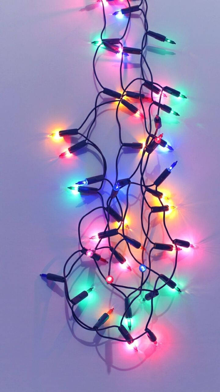 Christmas Lights Aesthetic 桌布 壁紙 — 一條纏繞的多色LED燈串，在純淺紫色背景上明亮發光。
