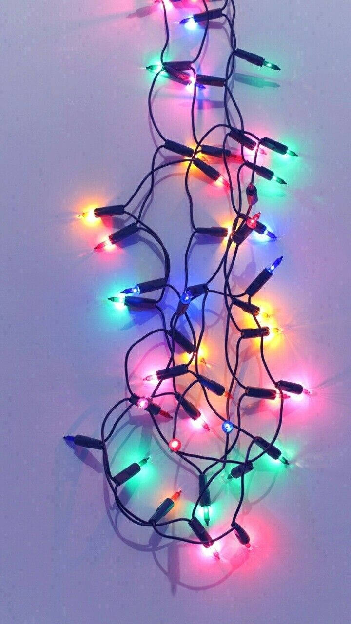 Christmas Lights Aesthetic 桌布 壁紙 — 一條纏繞著的彩色LED燈串，在純淺灰色背景上明亮地發光。