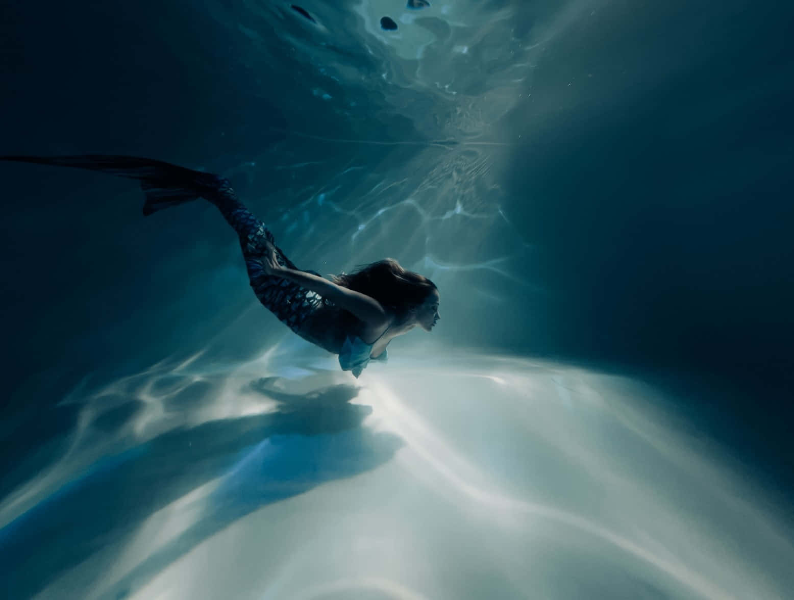 Real Mermaid 桌布 壁紙 — 一條美人魚在水底優雅地滑行，陽光穿過水面，在海底投射出閃爍的圖案。