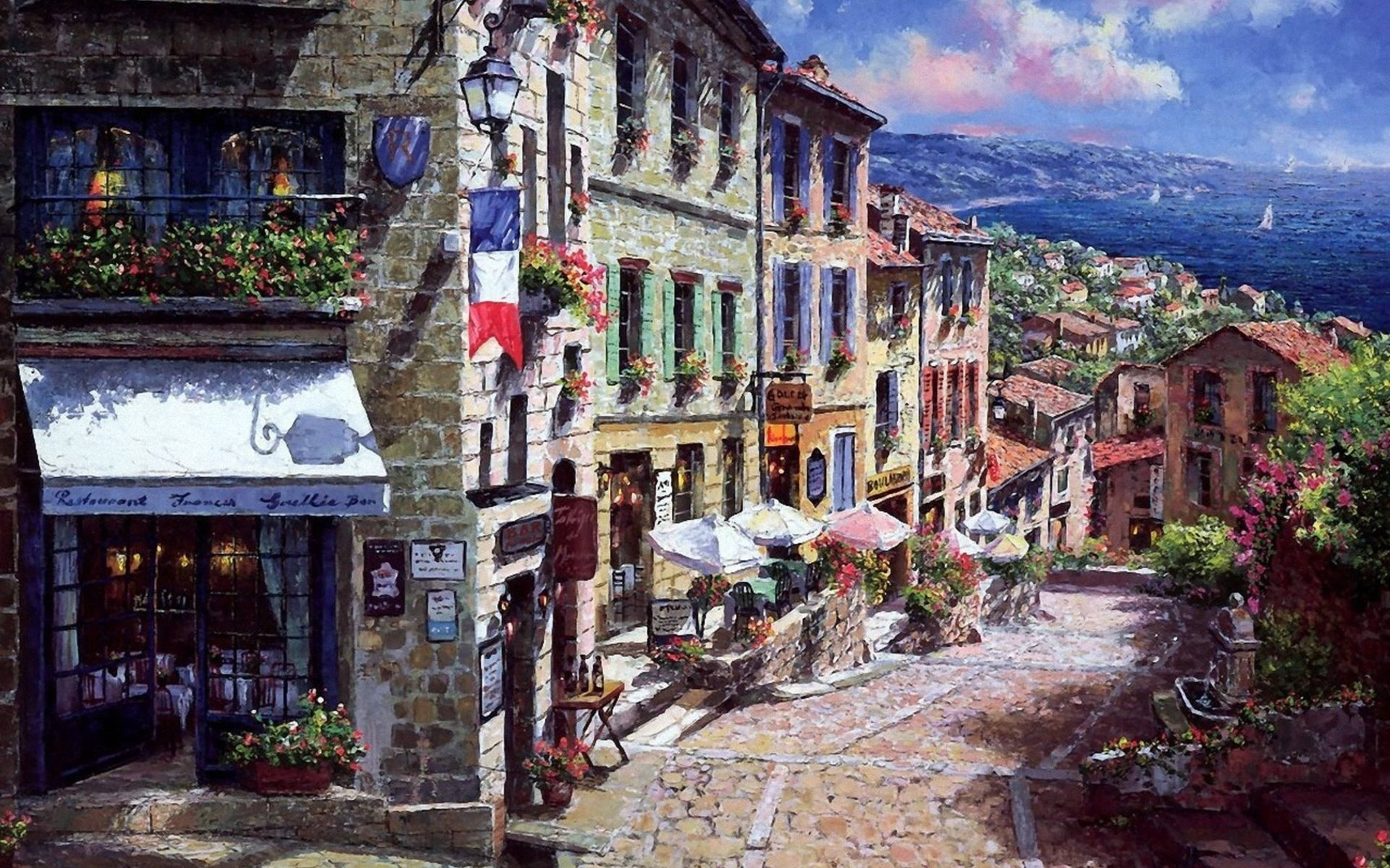 France Flag 桌布 壁紙 — 一條色彩繽紛的村莊街道，有石頭建築、花箱和一面法國國旗，俯瞰著藍色的大海。