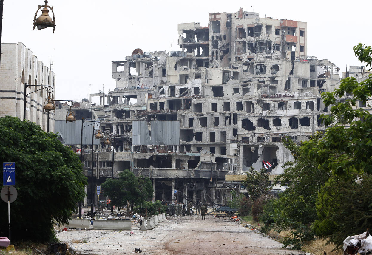 Syria 桌布 壁紙 — 一條荒涼的城市街道通向一棟嚴重受損的多層建築，窗戶破碎，鋼筋外露，在陰天的天空下被茂密的綠色植物環繞。