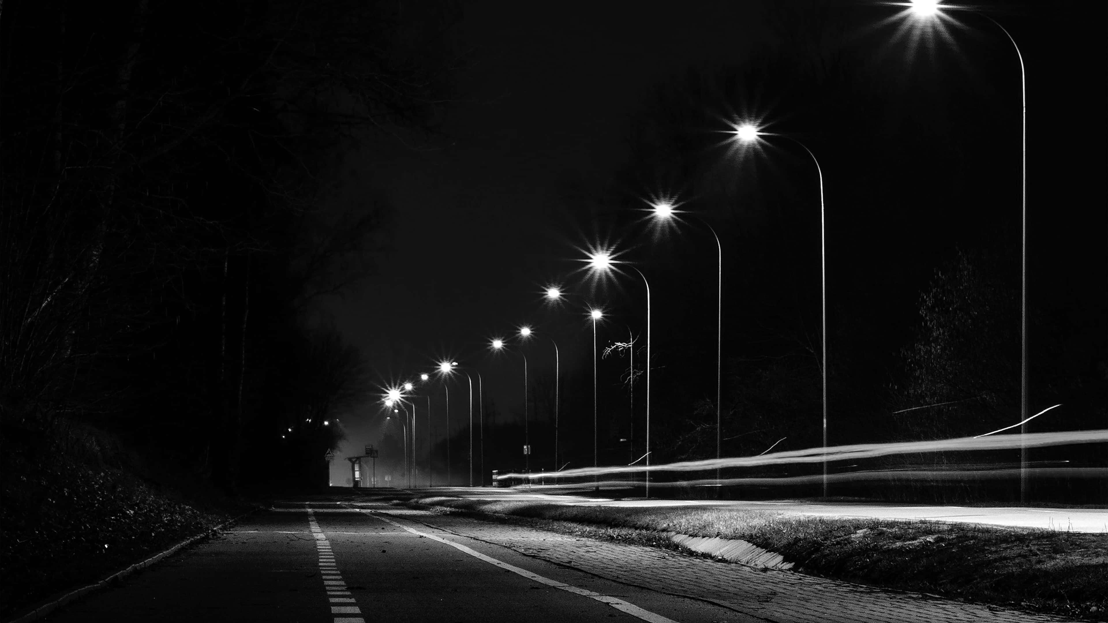 風景 桌布 壁紙 — 一條荒涼道路的黑白夜景，兩旁有發光的路燈和動態模糊的汽車軌跡。