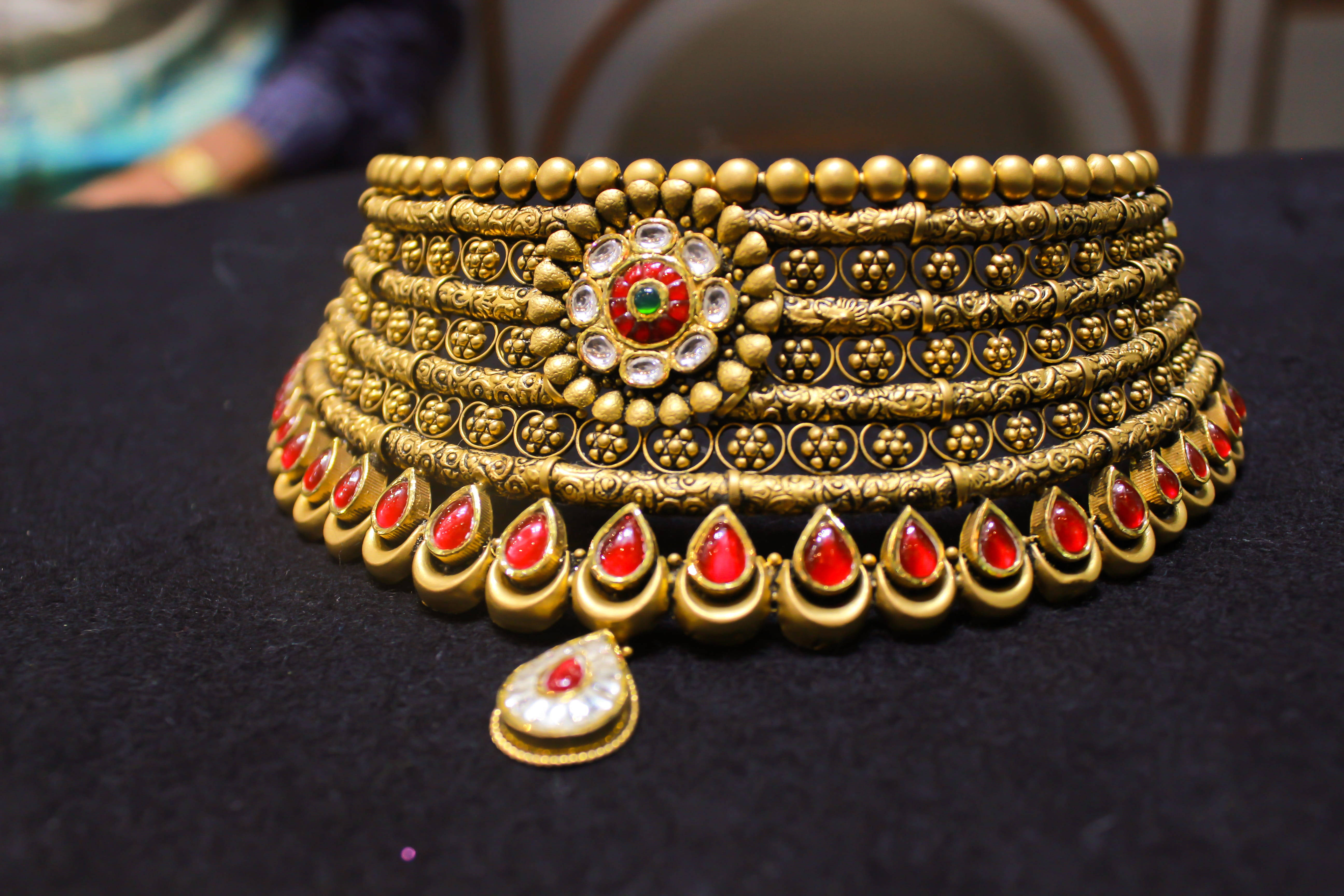 Gold Jewellery 桌布 壁紙 — 一條華麗的金色頸鏈，飾有紅色寶石和精緻圖案，放置在黑色天鵝絨表面上。